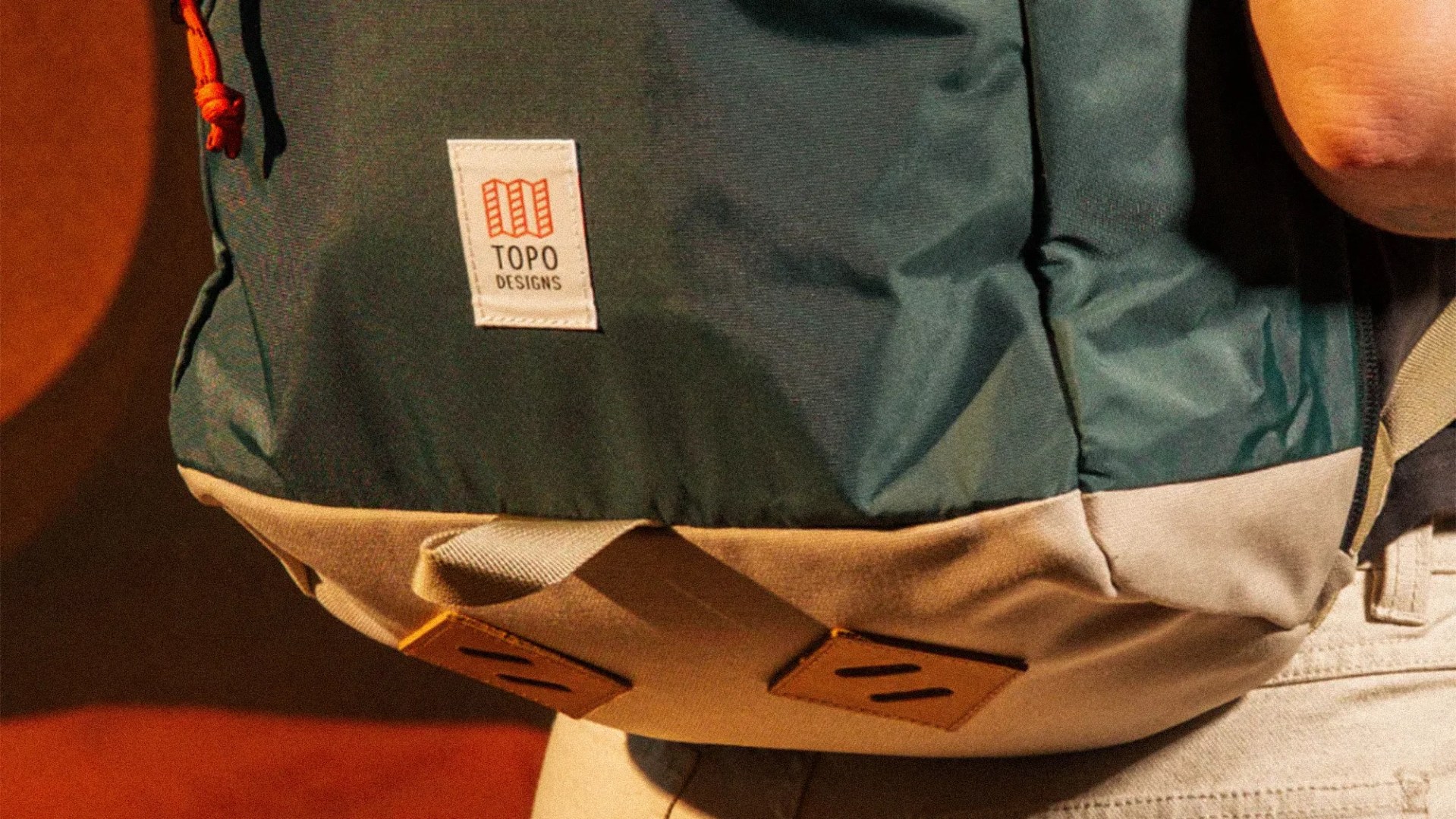 Close-up of a green and beige Topo Designs backpack with leather strap details and an orange drawstring.