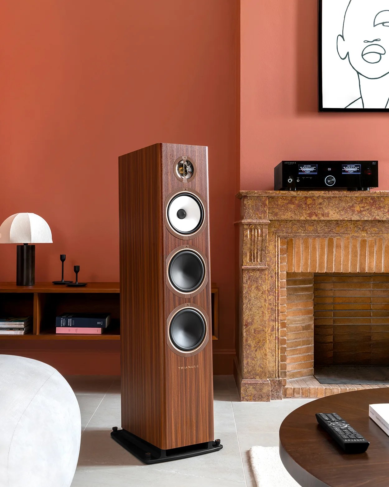 Tall wooden floor-standing speaker with three drivers and a black base in a living room.