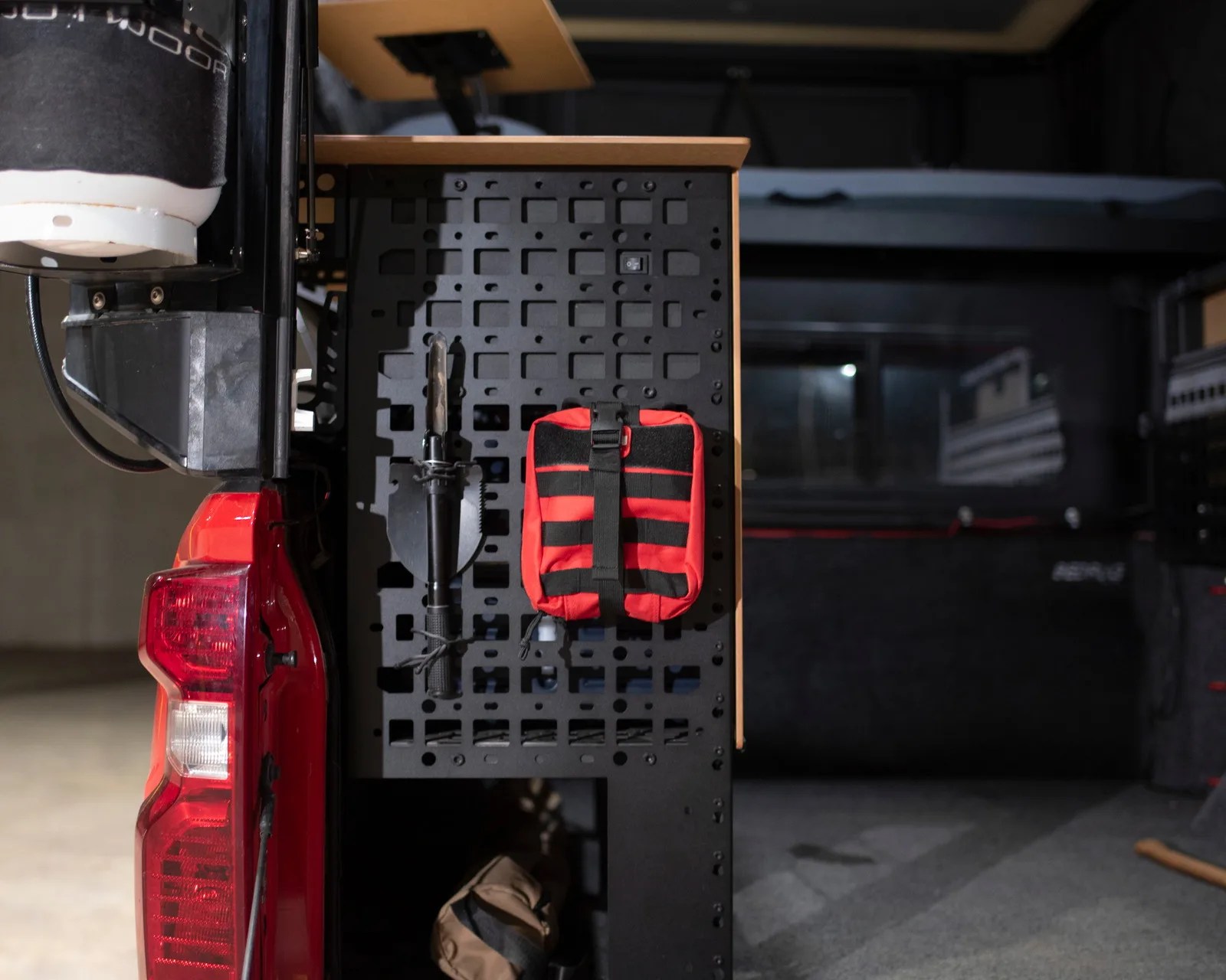 Black metal pegboard mounted on a red vehicle with a shovel and a red and black pouch attached.