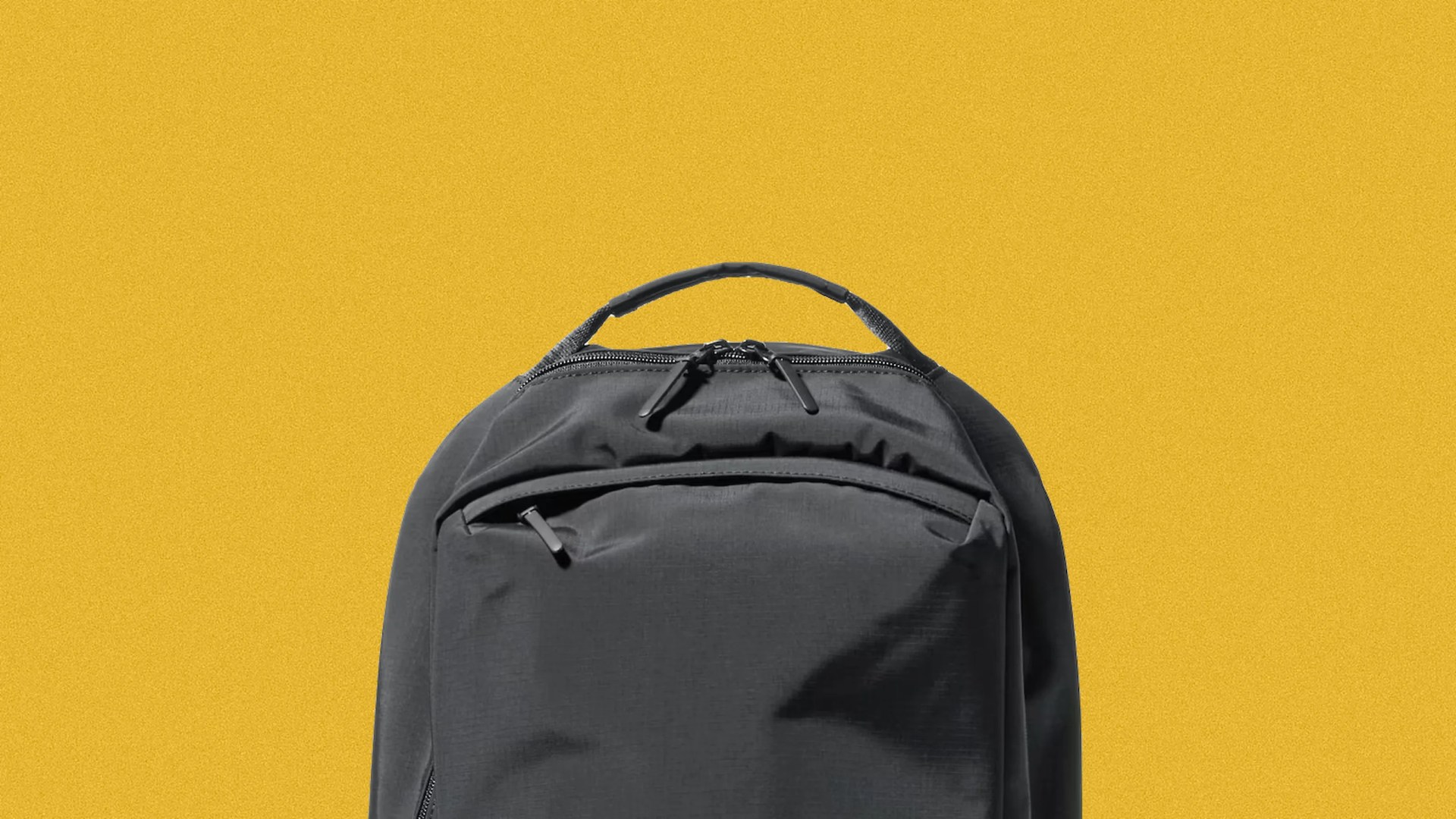 Black backpack with top handle and front zippered pocket against a yellow background.