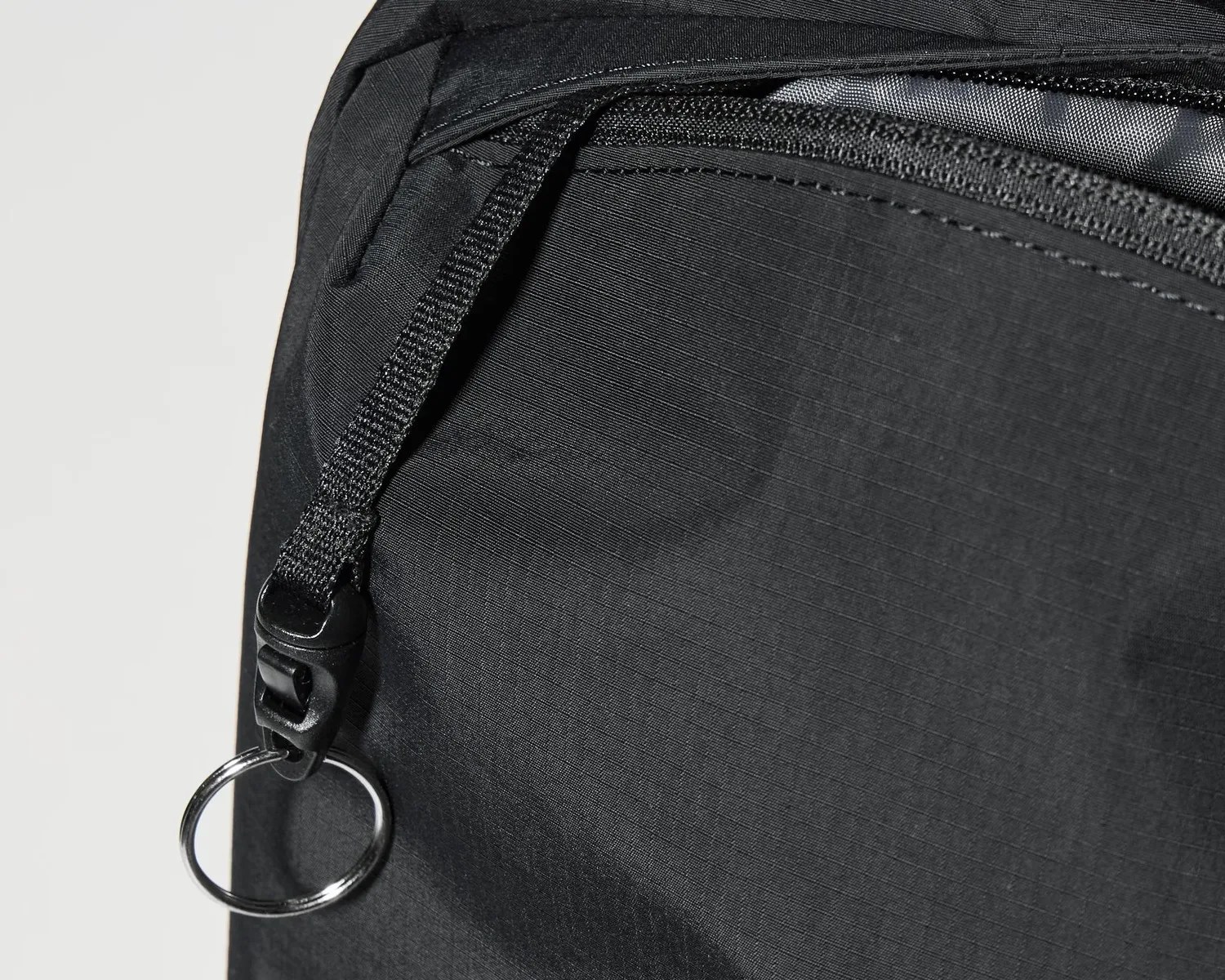 Close-up of a black fabric zipper pull with a black plastic clip and a silver keyring attached.