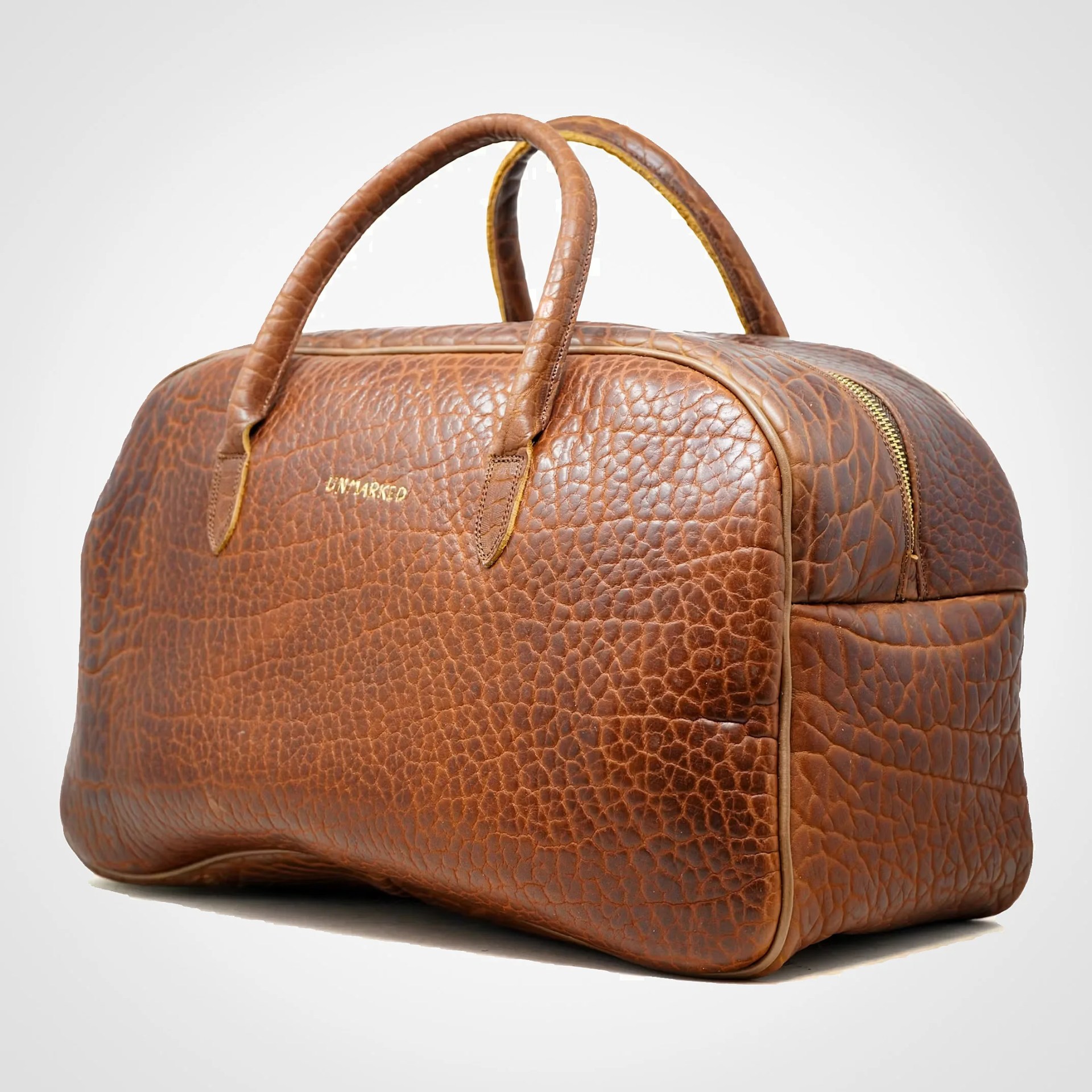 Brown textured leather duffel bag with rounded handles and gold zipper on a white background.