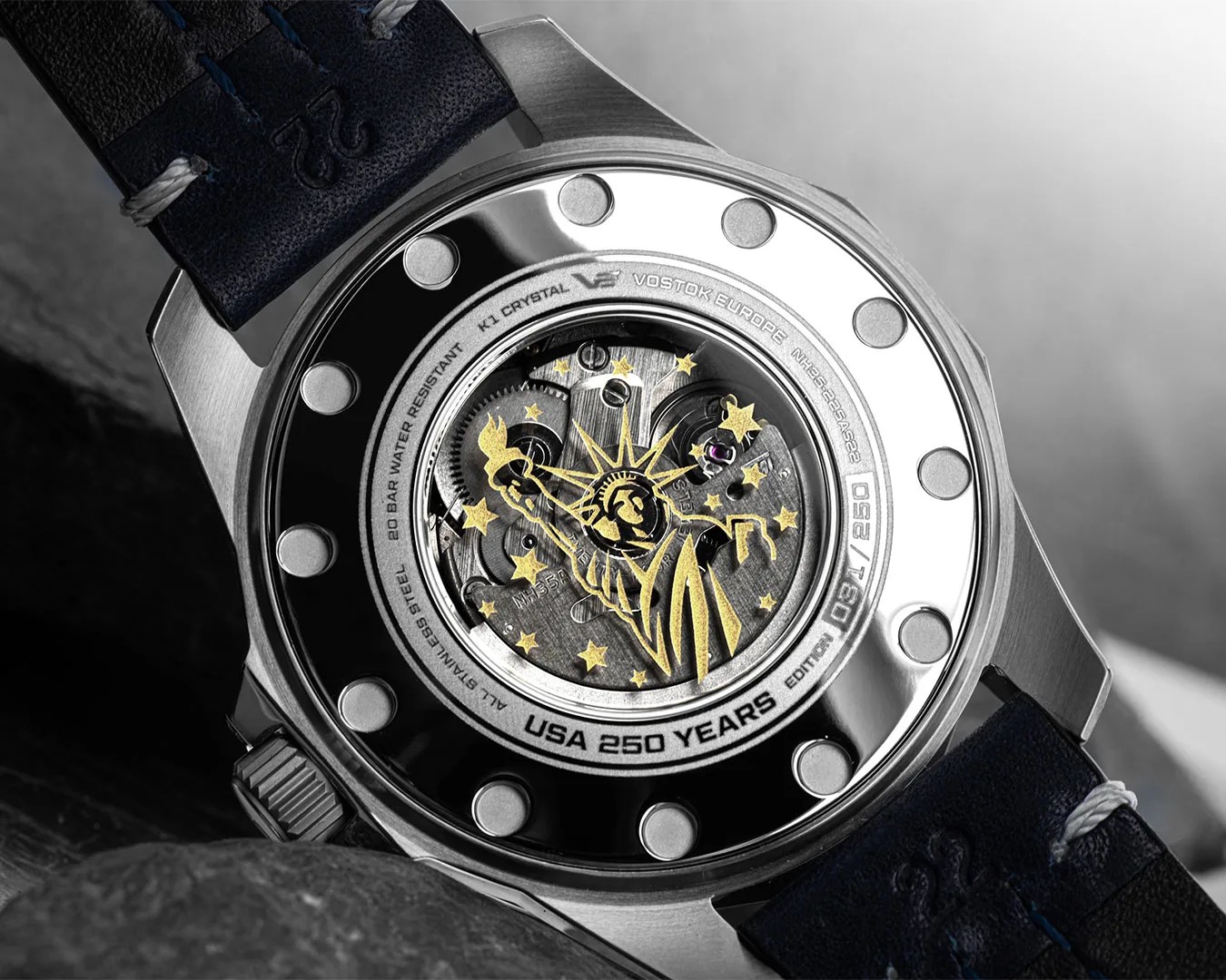 Back of a stainless steel Vostok Europe watch with visible mechanical movement and gold Statue of Liberty design.
