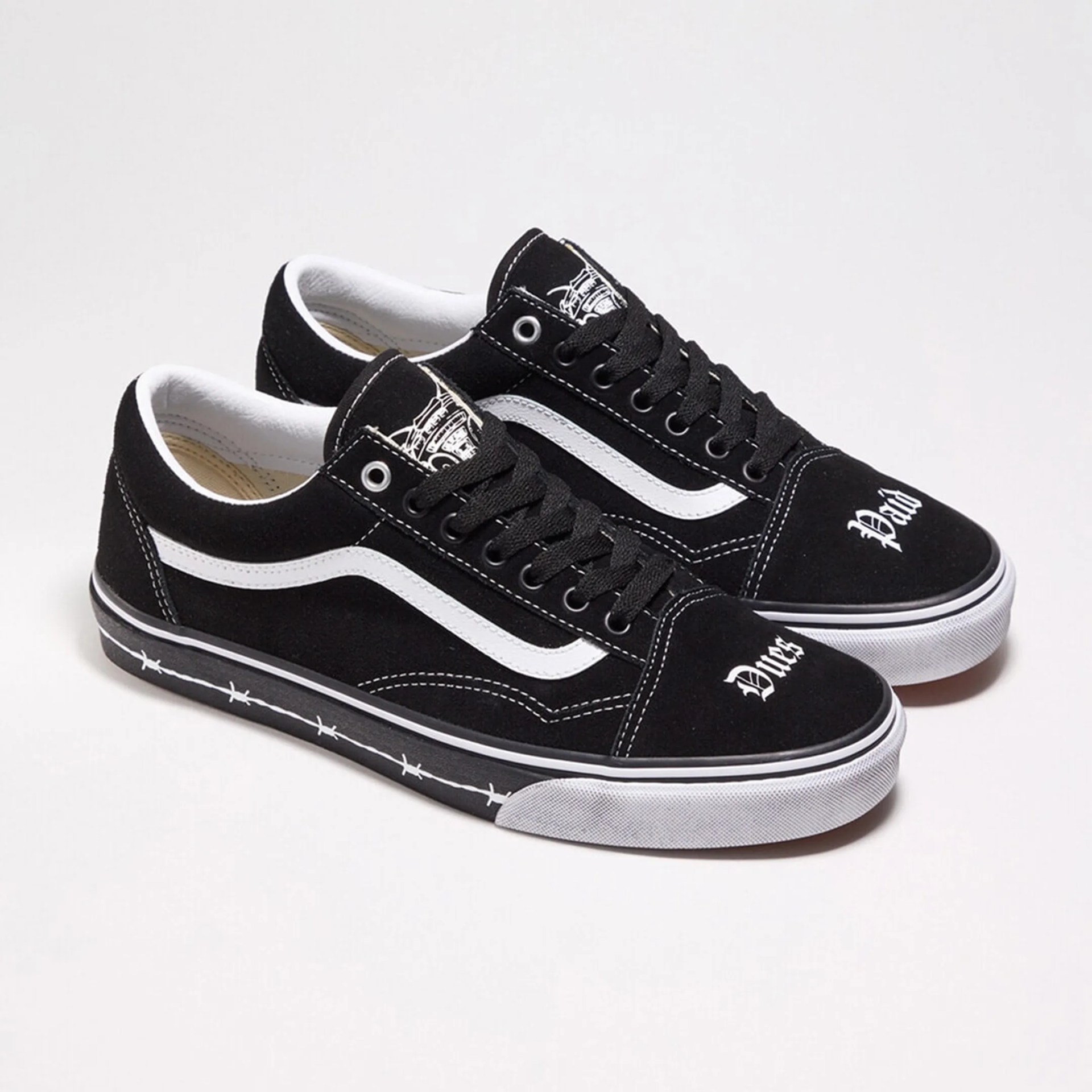 Pair of black Vans sneakers with white side stripe, white stitching, and barbed wire design on the sole edge.