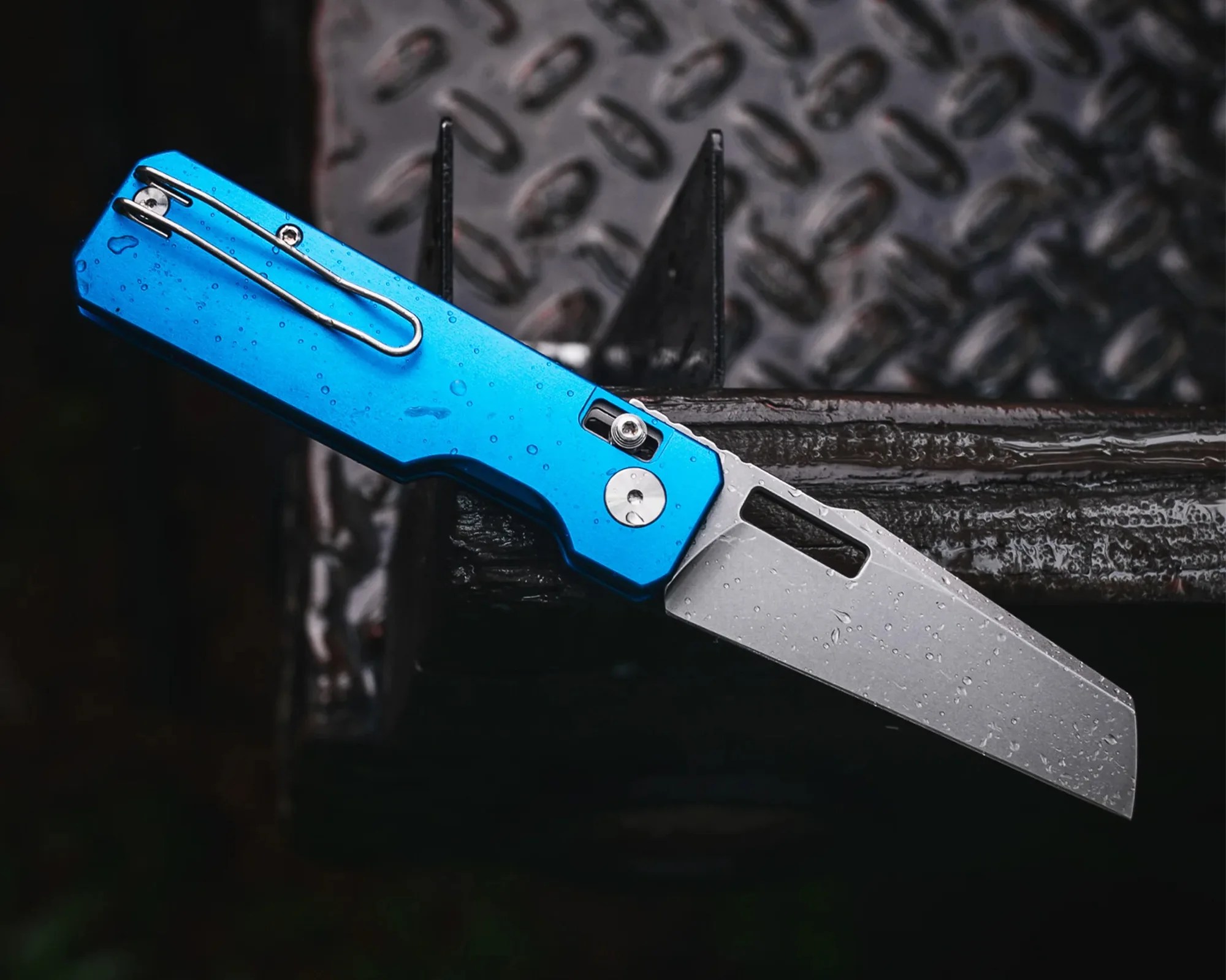 Blue-handled folding knife with a partially serrated silver blade and water droplets on it.