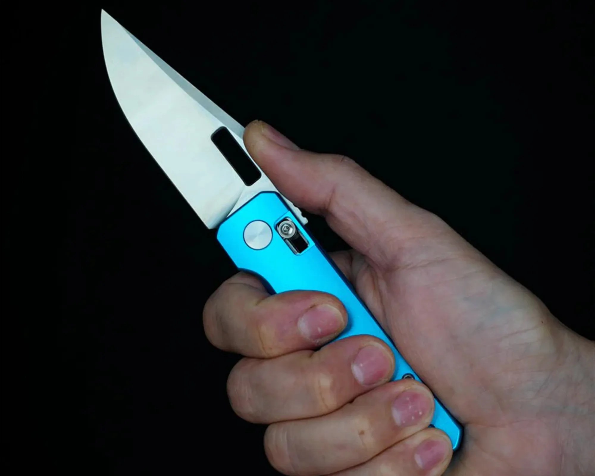 Hand holding a blue folding knife with a silver blade against a black background.