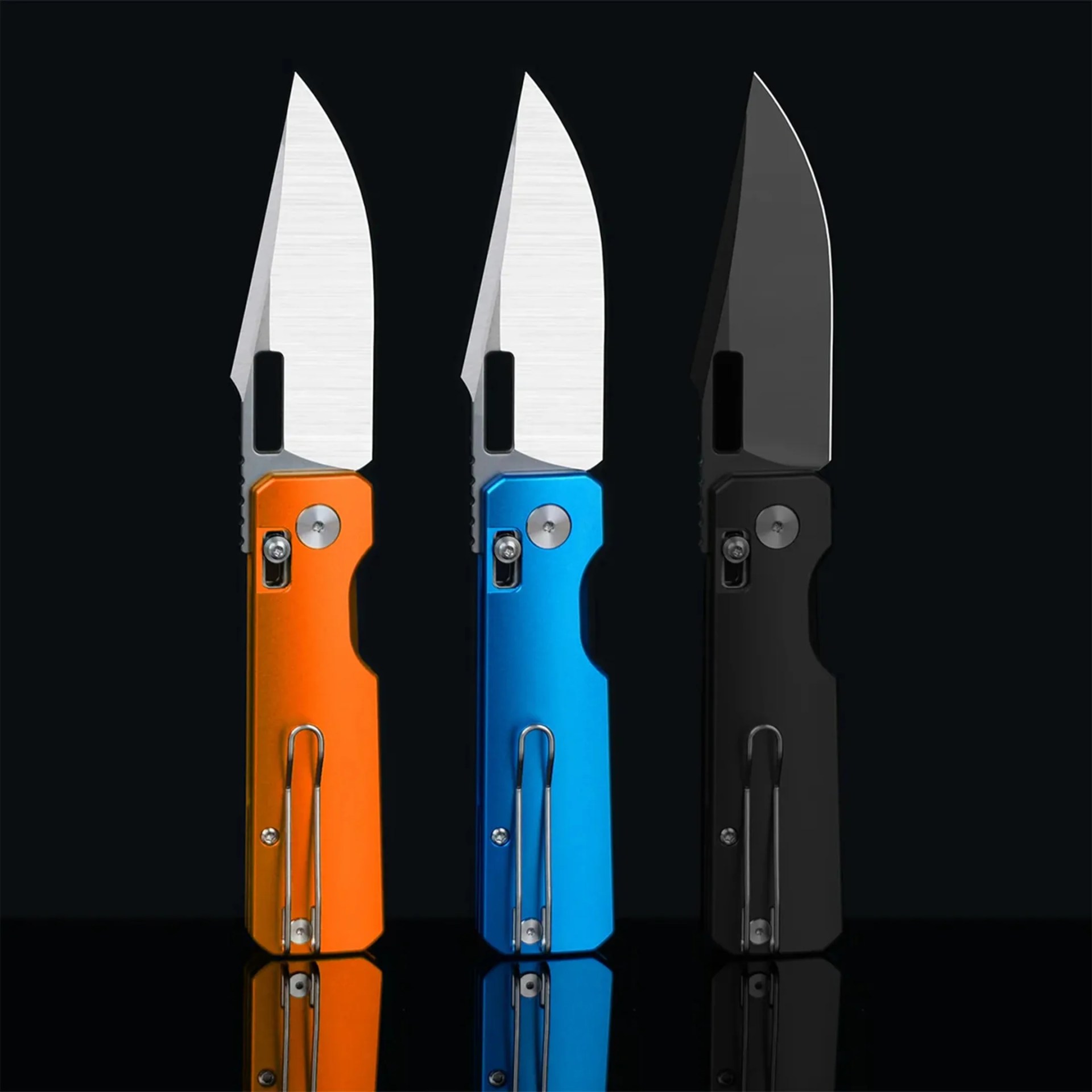 Three folding knives with partially serrated blades and handles in orange, blue, and black, reflected on a black surface.