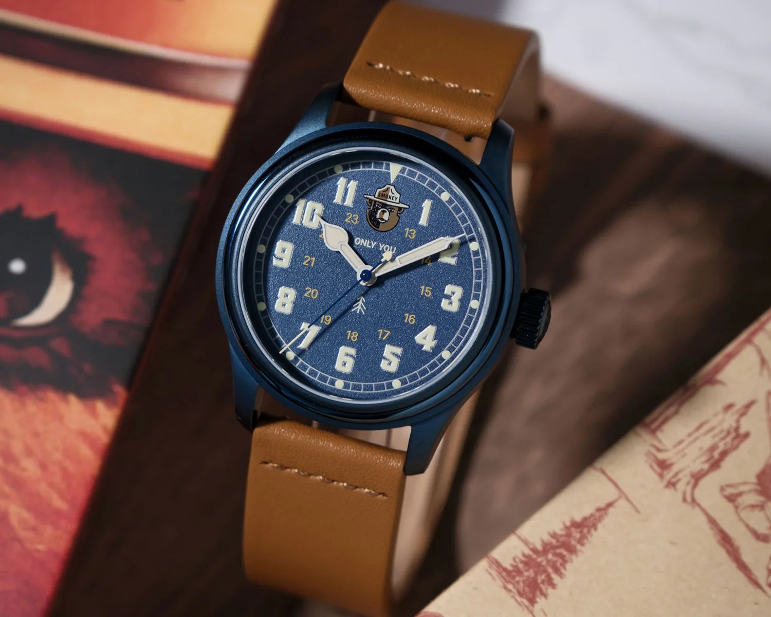 Blue watch with tan leather strap and a Smokey Bear logo on the dial showing 1:10:37.