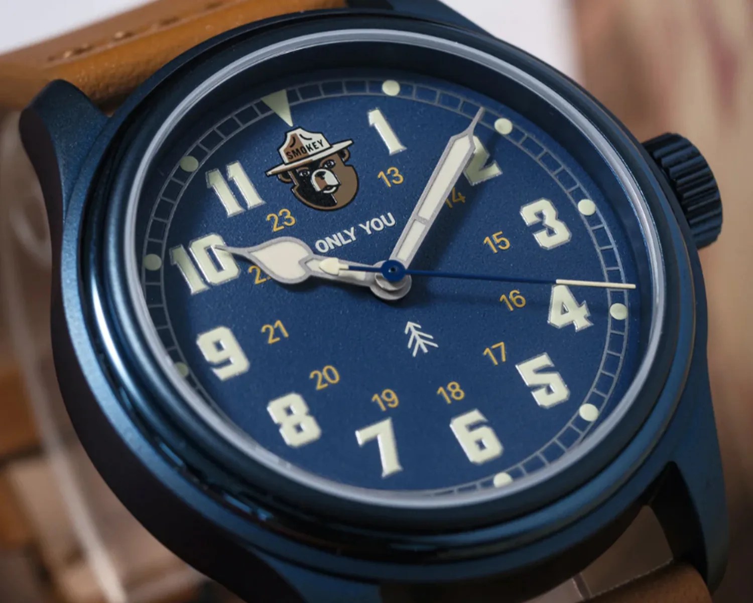 Close-up of a blue watch face with large white numbers, a Smokey Bear logo, and a brown leather strap.