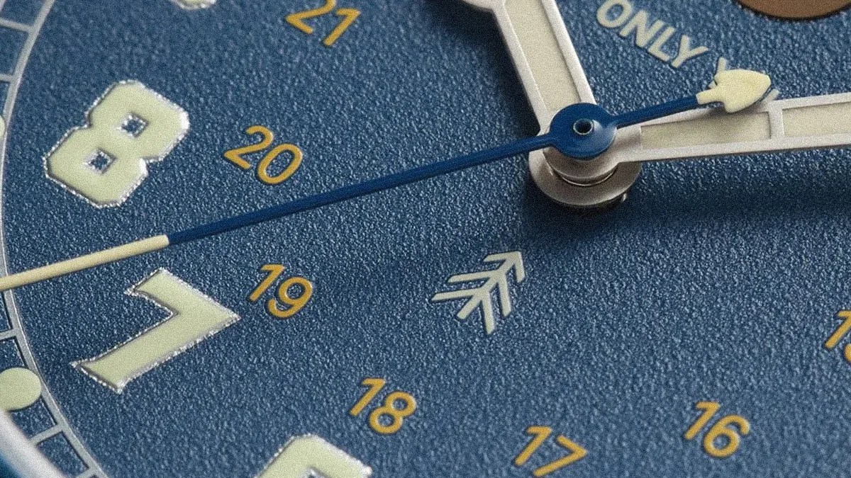 Close-up of a blue watch face showing white hour and minute hands, a blue second hand, and yellow numbers 16 to 21.