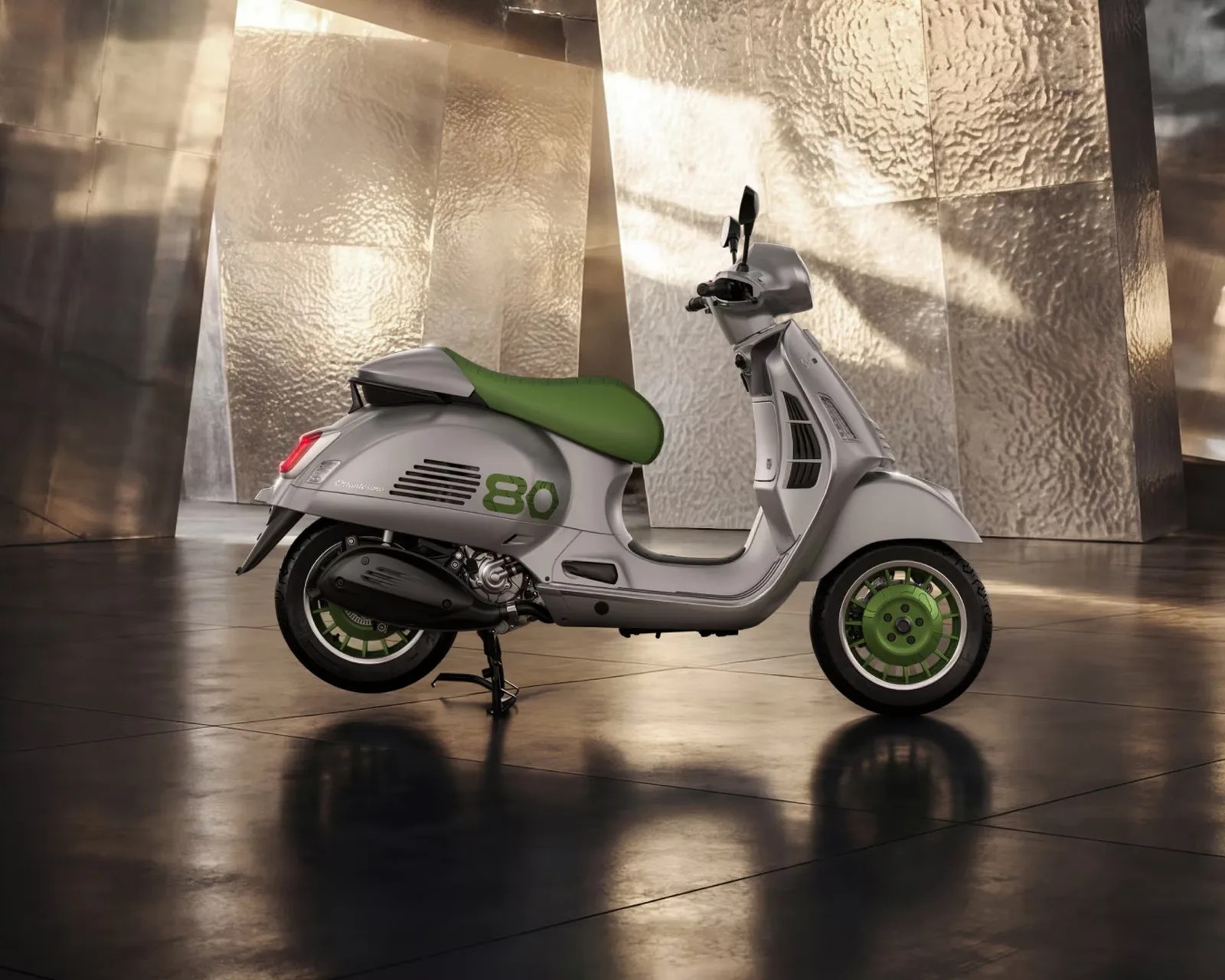 Silver scooter with green seat and green wheel hubs parked indoors on a reflective floor.