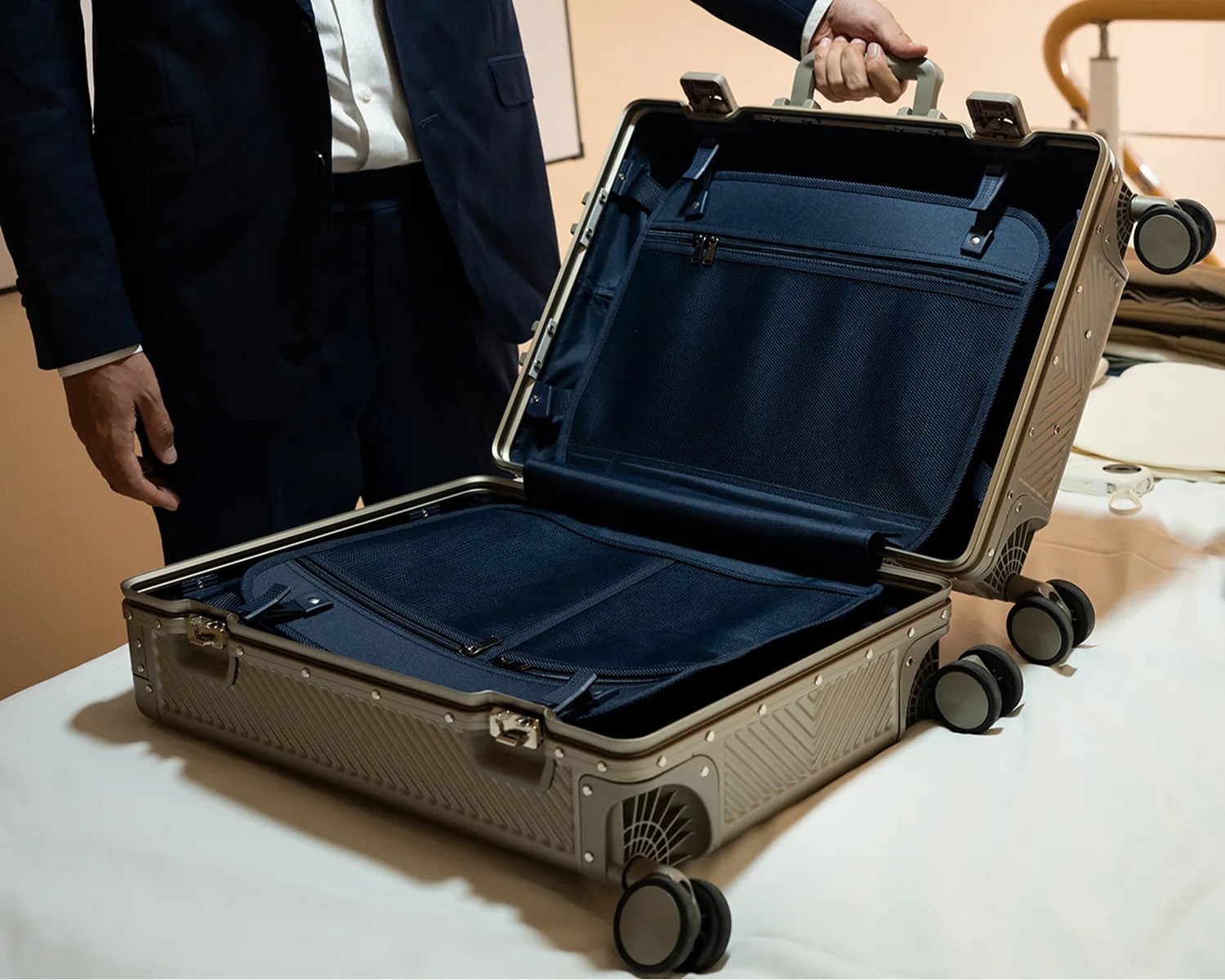 Open silver hard-shell suitcase with black fabric interior compartments and four wheels on a white surface.