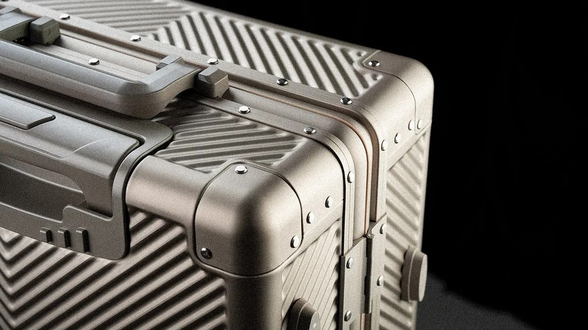 Close-up of a metallic silver hard-shell suitcase corner with diagonal ridges and riveted edges against a black background.