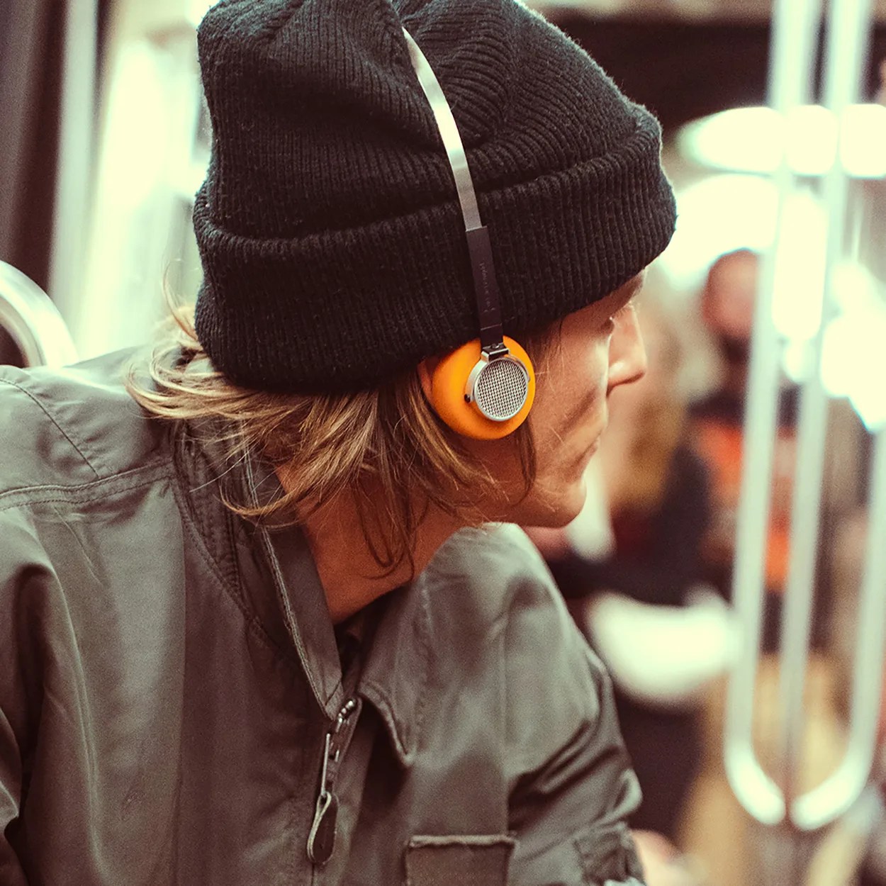 Person wearing orange and silver headphones with a black knit beanie and green jacket.