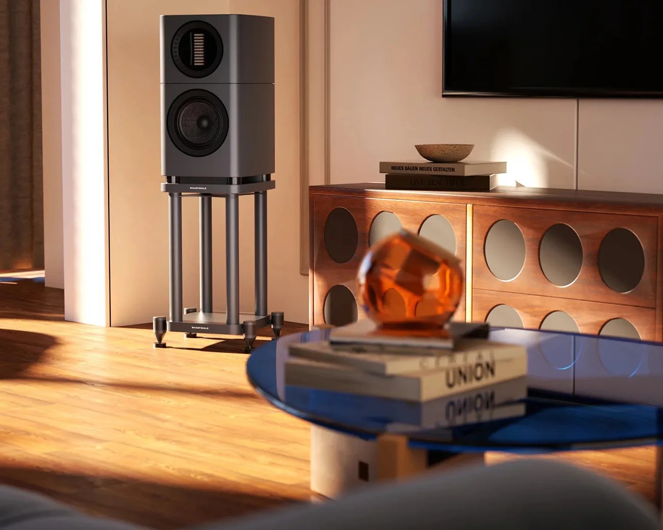 Gray Wharfedale speaker on a matching stand in a sunlit room with wooden floor and a blue glass table.
