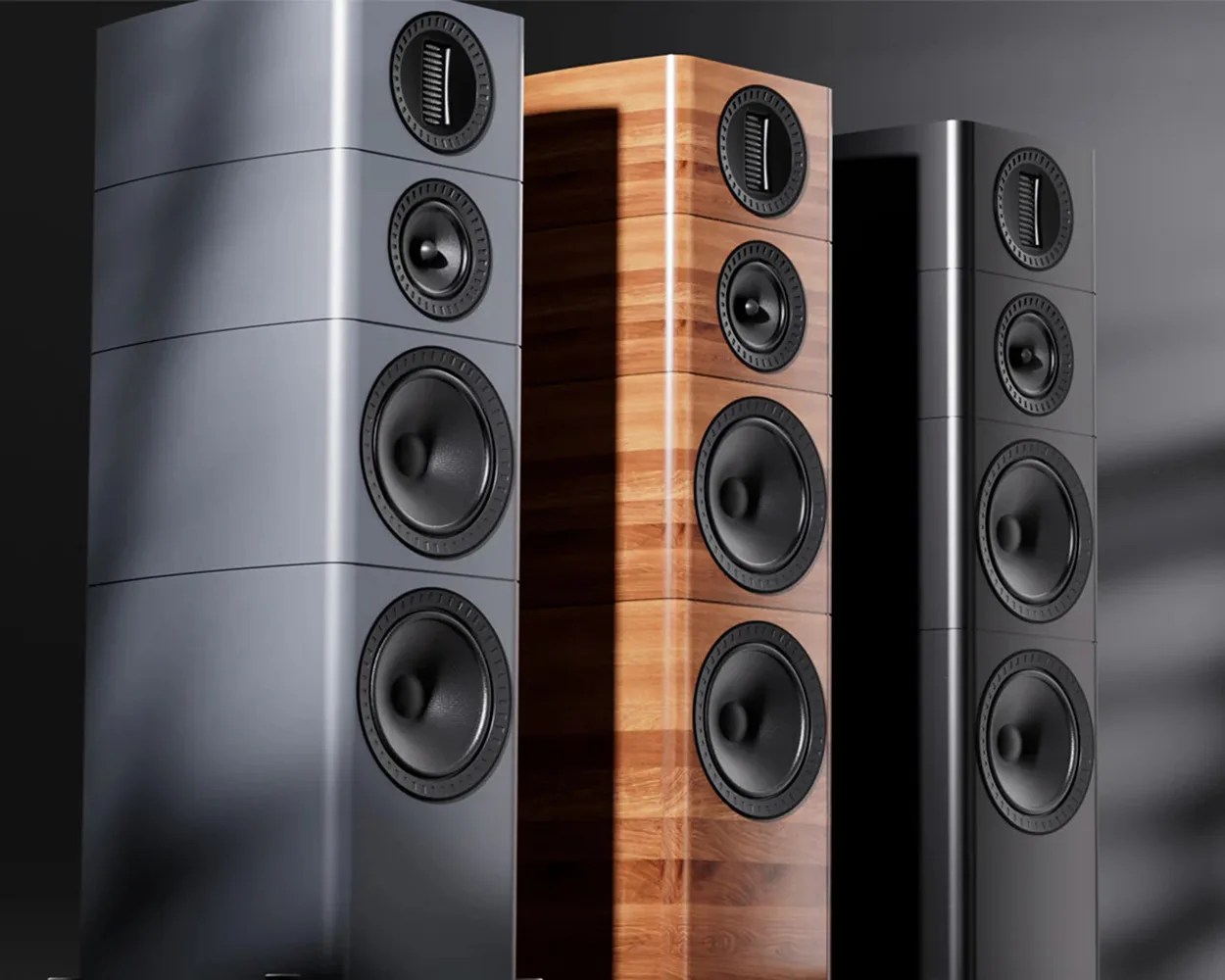 Three tall floor-standing speakers with four drivers each, in matte gray, wood finish, and glossy black finishes.
