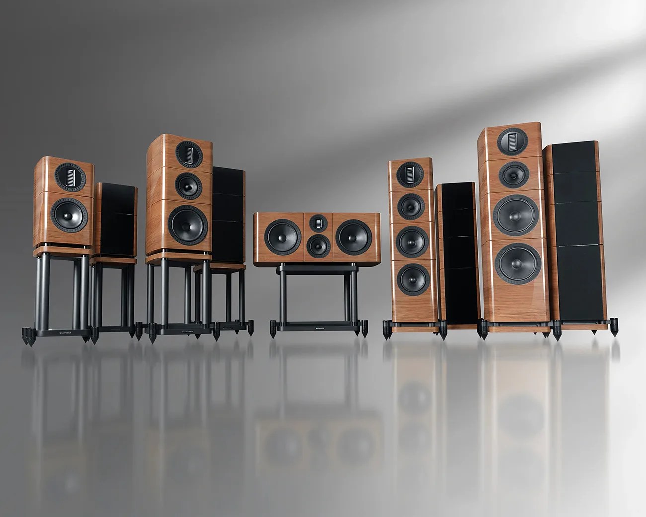 Set of six wooden speakers with black drivers and stands, arranged on a reflective gray surface.