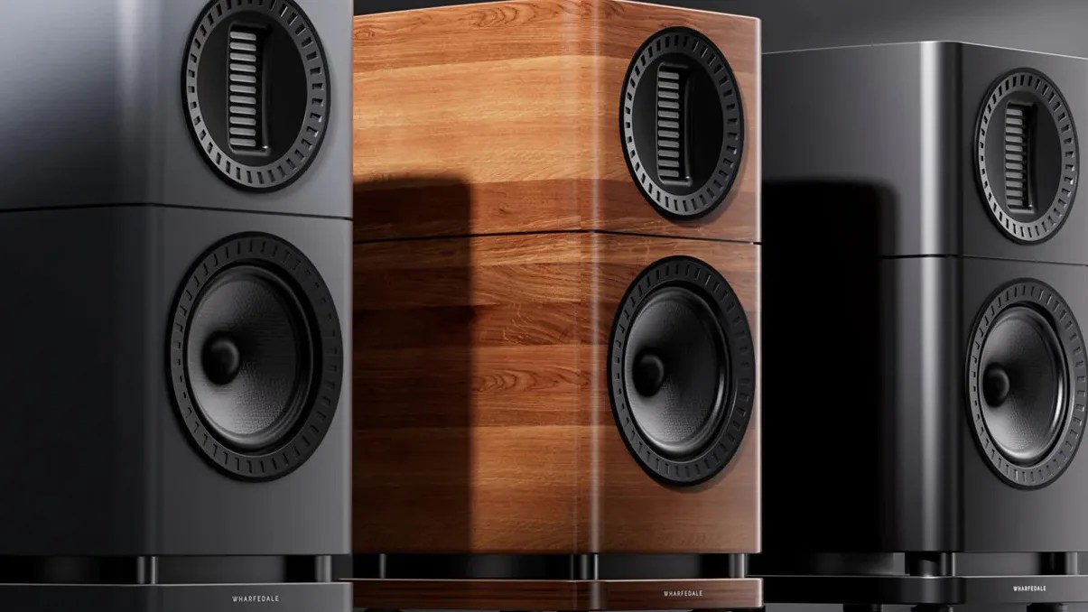 Three Wharfedale speakers in black matte, wood finish, and glossy black finishes, each with two circular drivers.