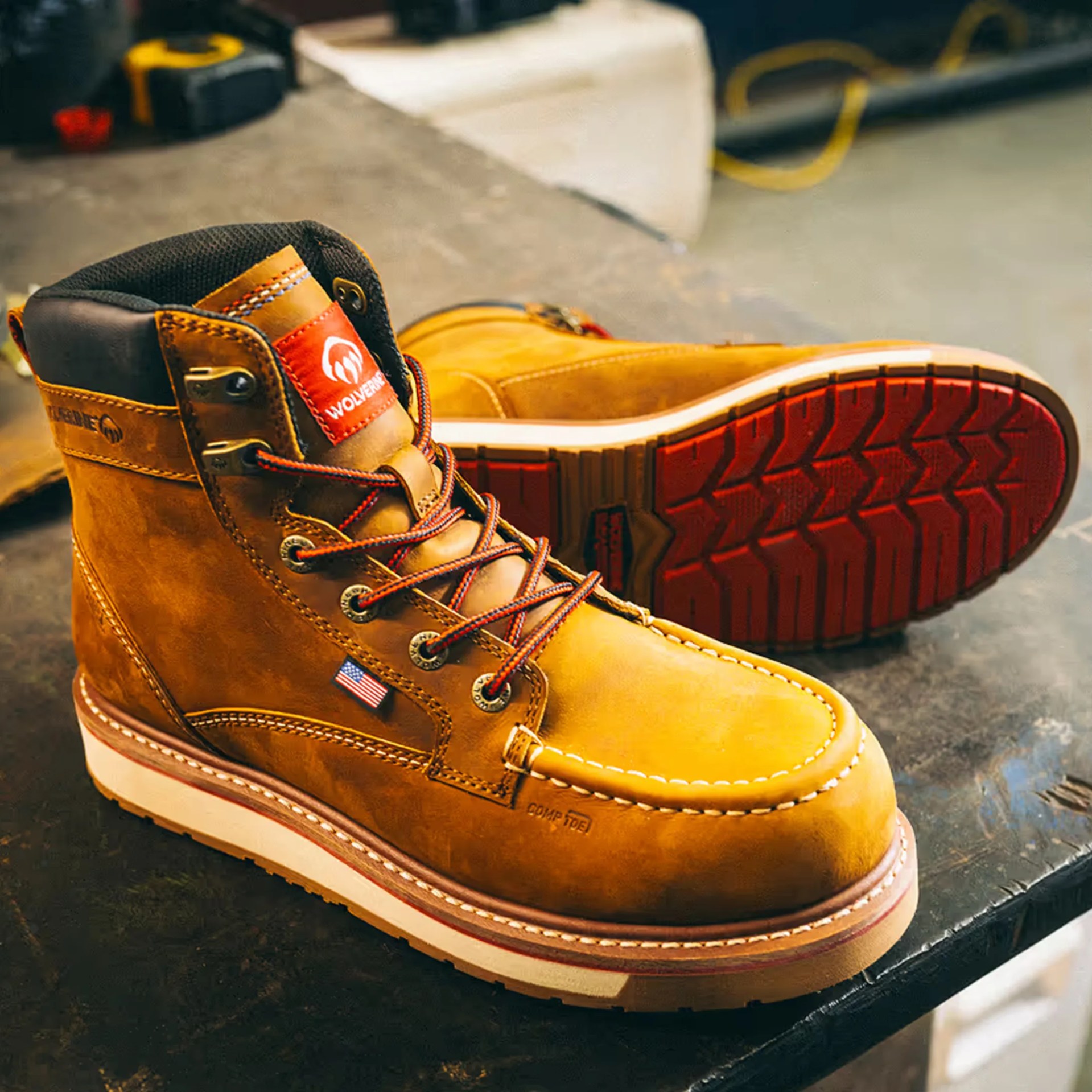 Brown leather Wolverine work boot with red and black laces and red tread sole on a dark surface.