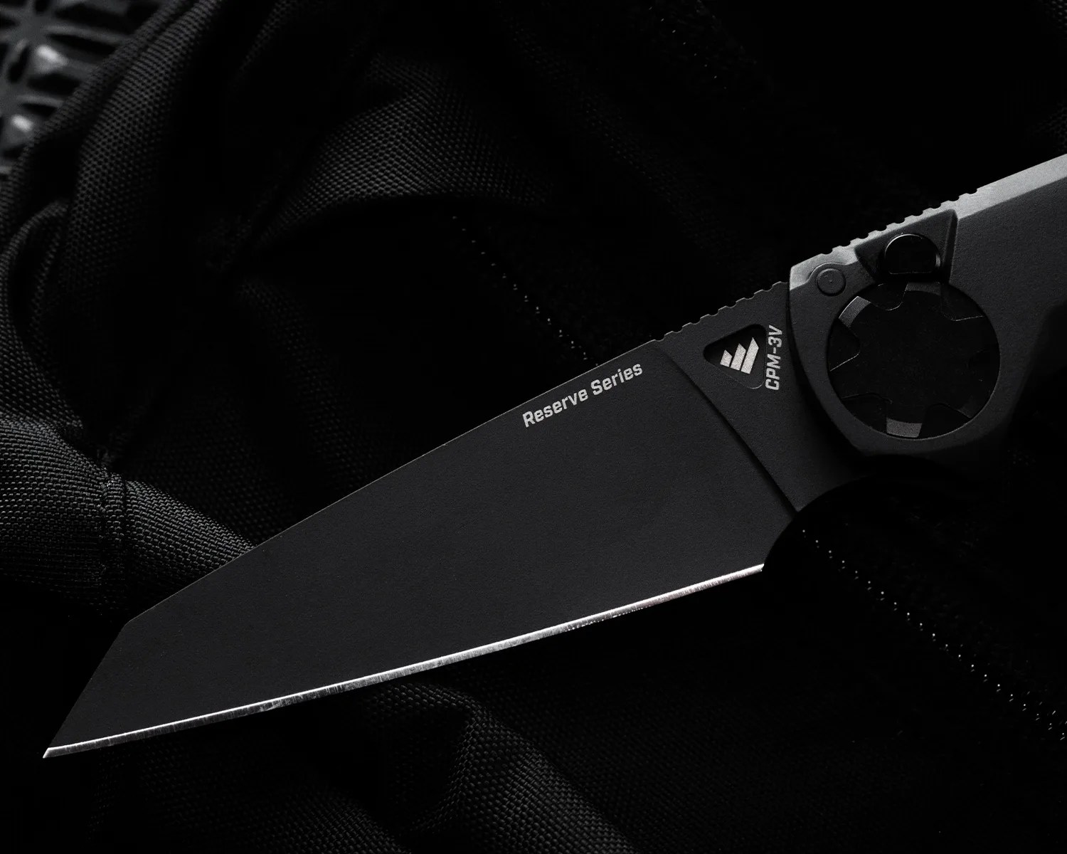 Black folding knife blade with "Reserve Series" and "CPM-3V" markings on a black fabric background.