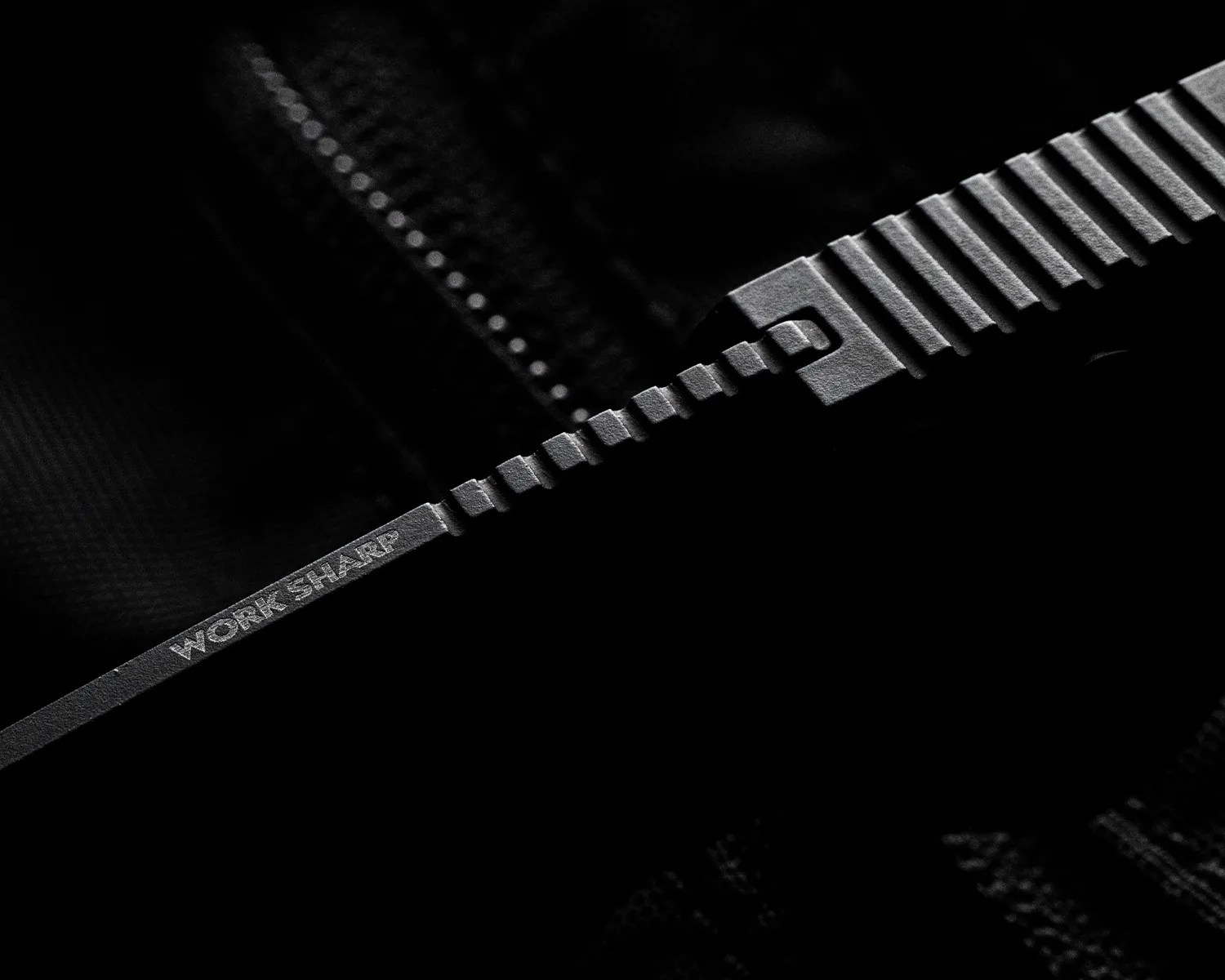 Close-up of a black serrated knife blade with the words "WORK SHARP" engraved on it.