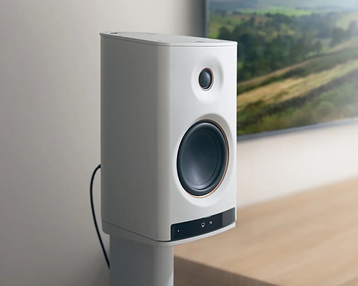 White bookshelf speaker with black drivers and a black control panel at the bottom, placed on a stand near a TV.