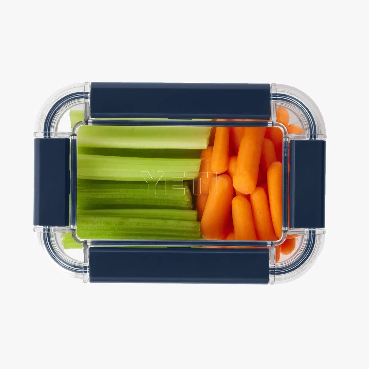Clear rectangular YETI container with navy blue latches holding celery sticks and baby carrots.