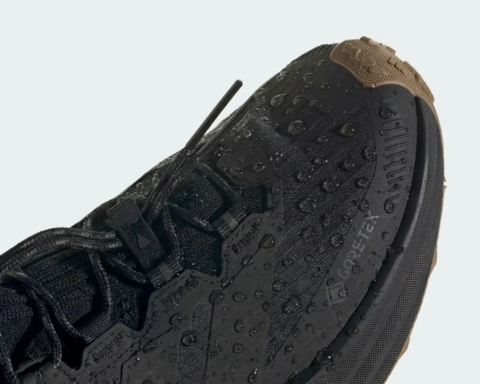 Close-up of a black Gore-Tex shoe with water droplets on its surface and a brown textured toe cap.