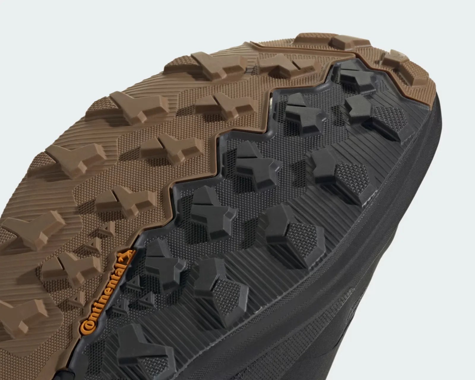Close-up of a black and brown rugged shoe sole with deep, multi-directional lugs and a small orange "Continental" logo.