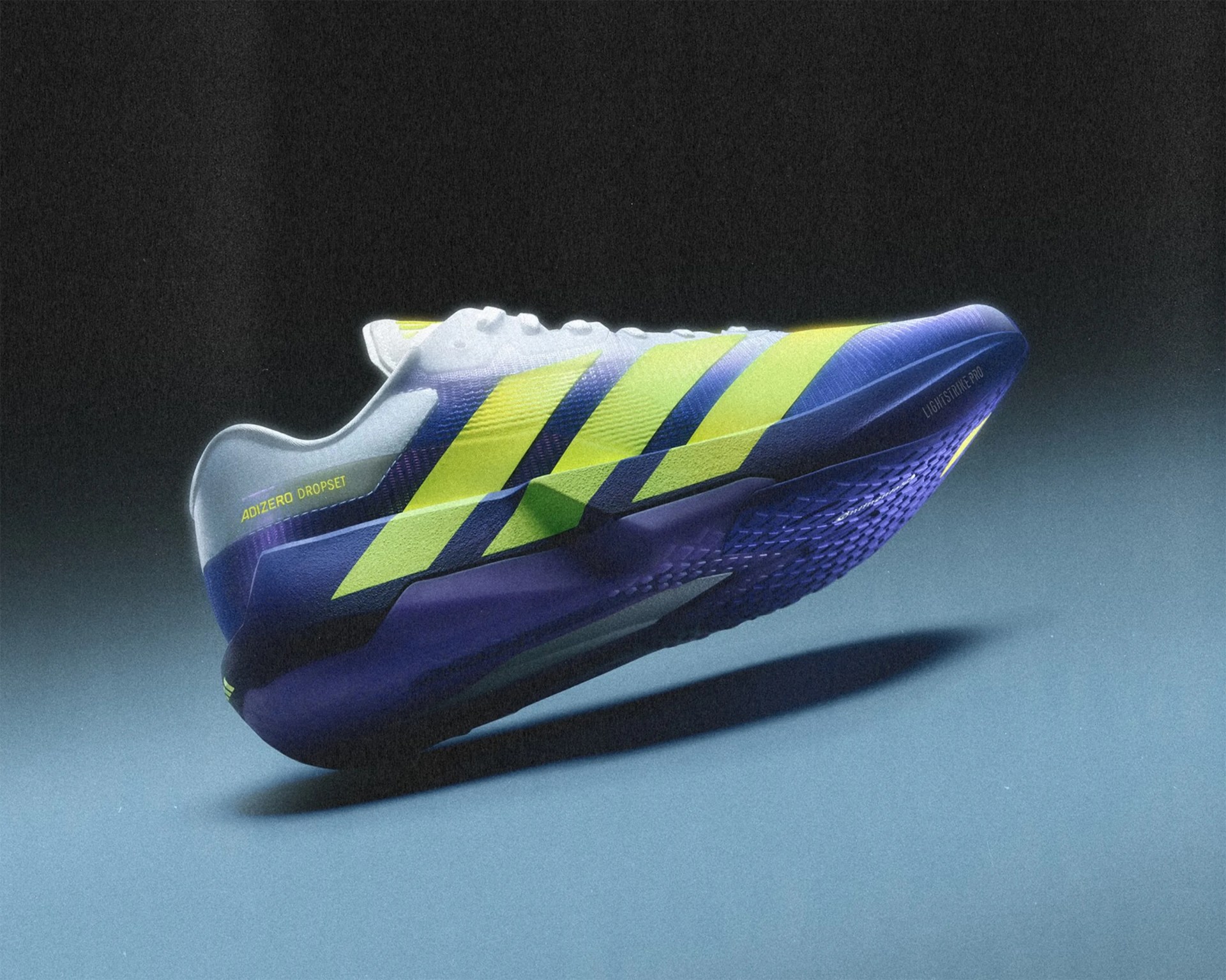 Purple and yellow Adidas Adizero DropSet running shoe with white laces on a blue surface.