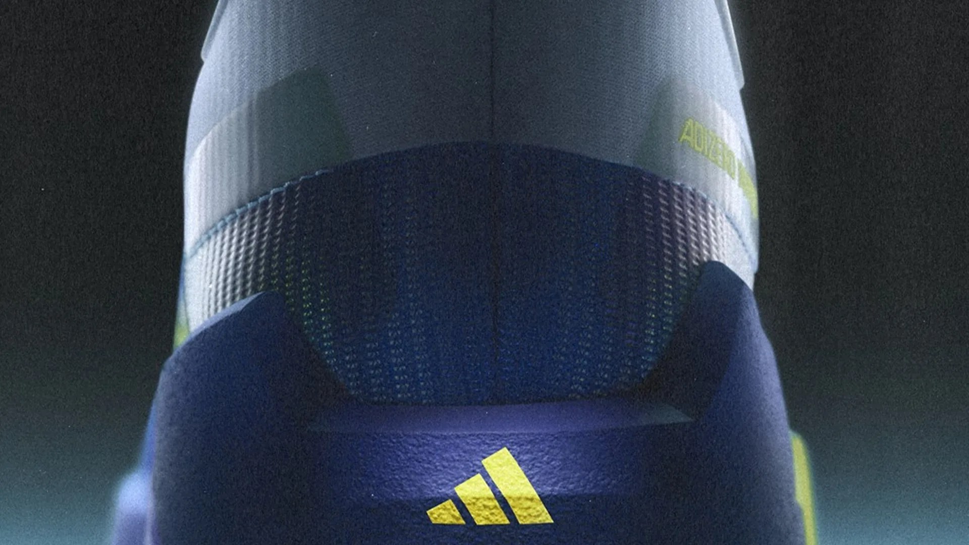 Close-up of the heel area of a blue Adidas shoe with yellow logo and textured knit fabric.