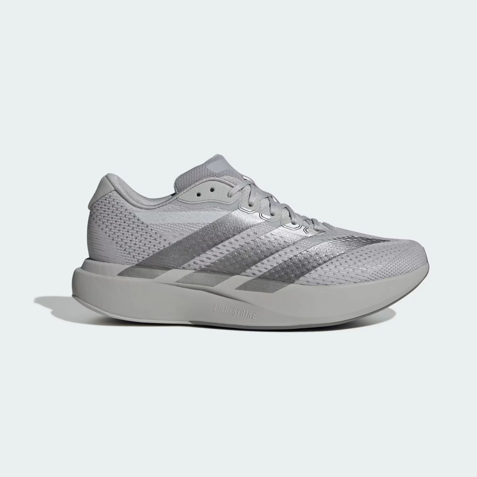 Light gray athletic shoe with mesh upper, three metallic stripes, and thick cushioned sole labeled "Lightstrike.