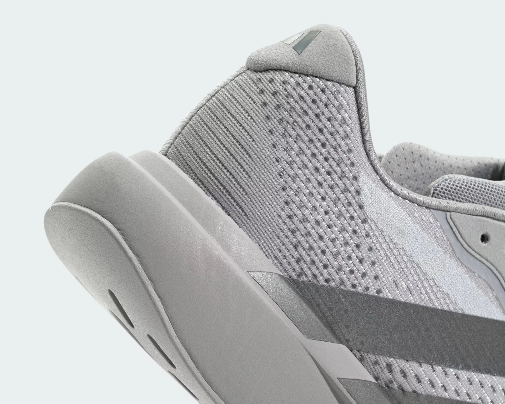 Close-up of a light gray sneaker heel with knit fabric and suede accents on a white background.