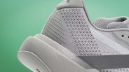 Close-up of the heel and side of a light gray athletic shoe with mesh and suede textures against a green background.