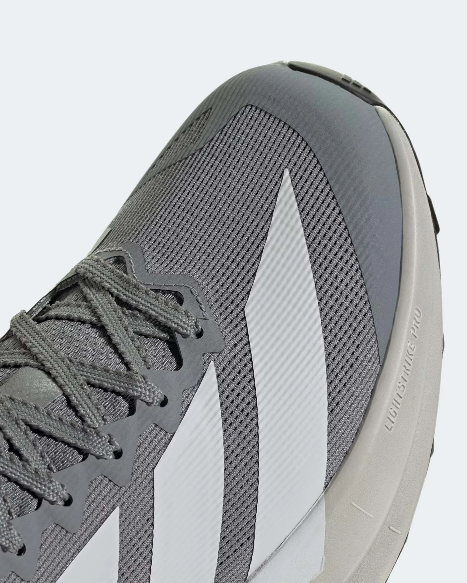 Close-up of a gray mesh sneaker with white stripes and gray laces, featuring a light beige sole with "LIGHTSTRIKE PRO" text.