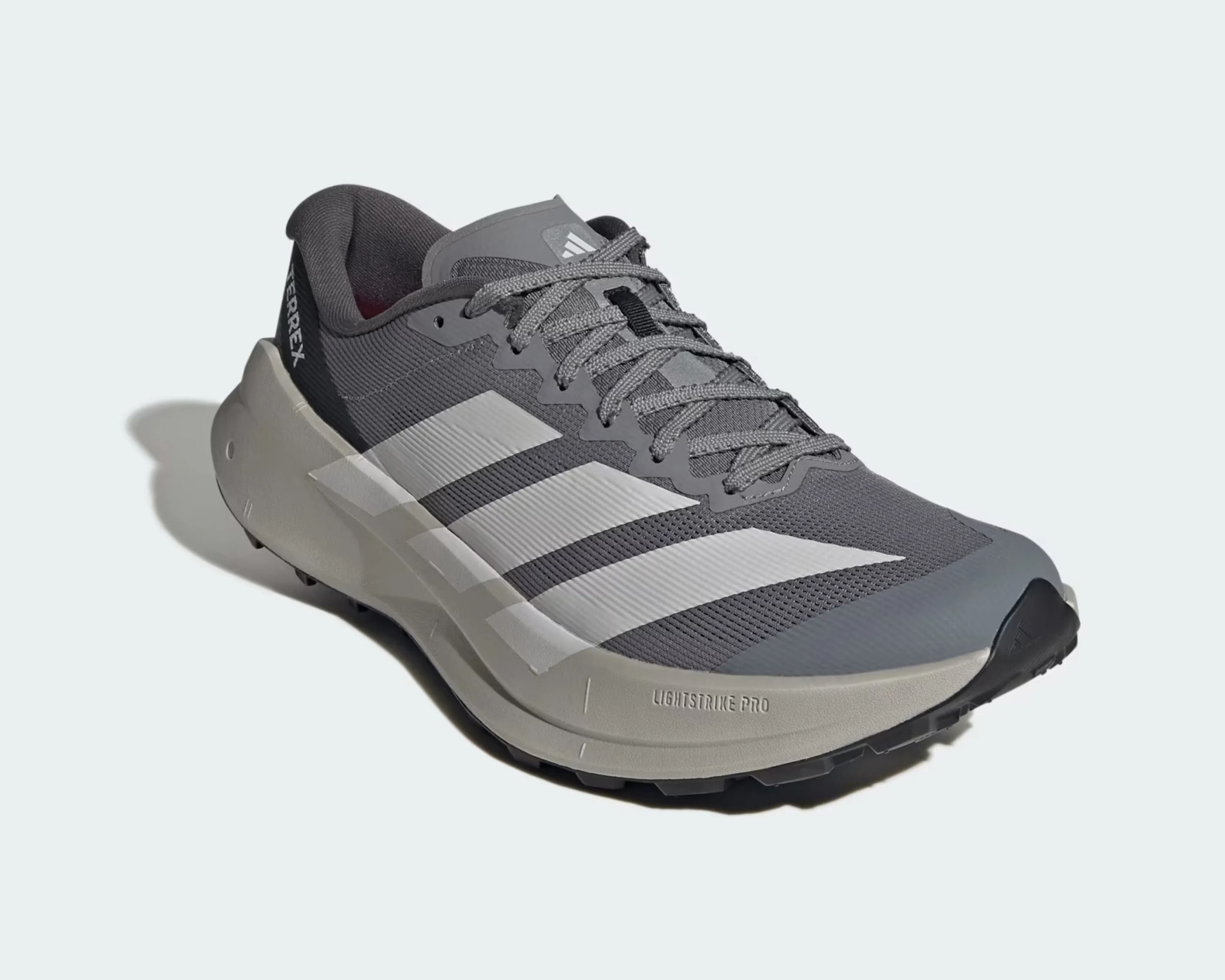 Gray Adidas Terrex trail running shoe with white stripes and beige Lightstrike Pro sole.