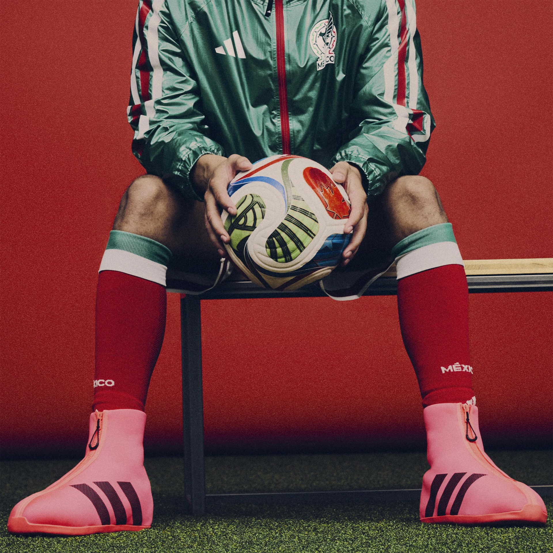 Pink soccer cleats with black stripes worn by a person sitting on a bench holding a colorful soccer ball.