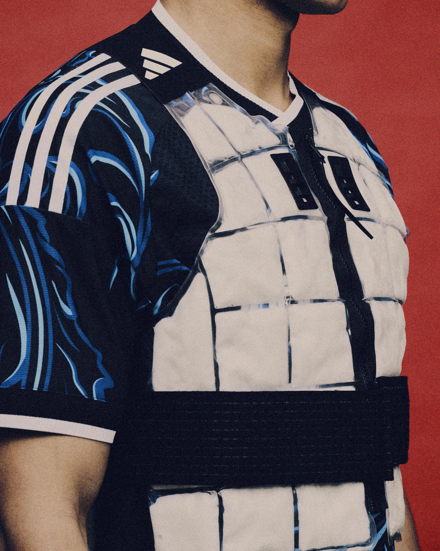 Black and blue Adidas sports shirt with white stripes worn under a white padded vest with black straps.