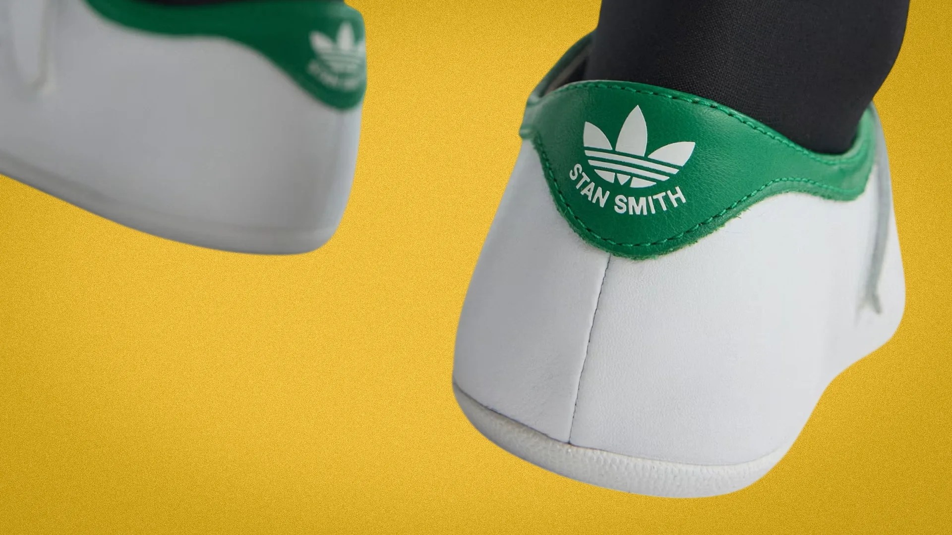 White Adidas Stan Smith sneakers with green heel tab and logo on a yellow background.