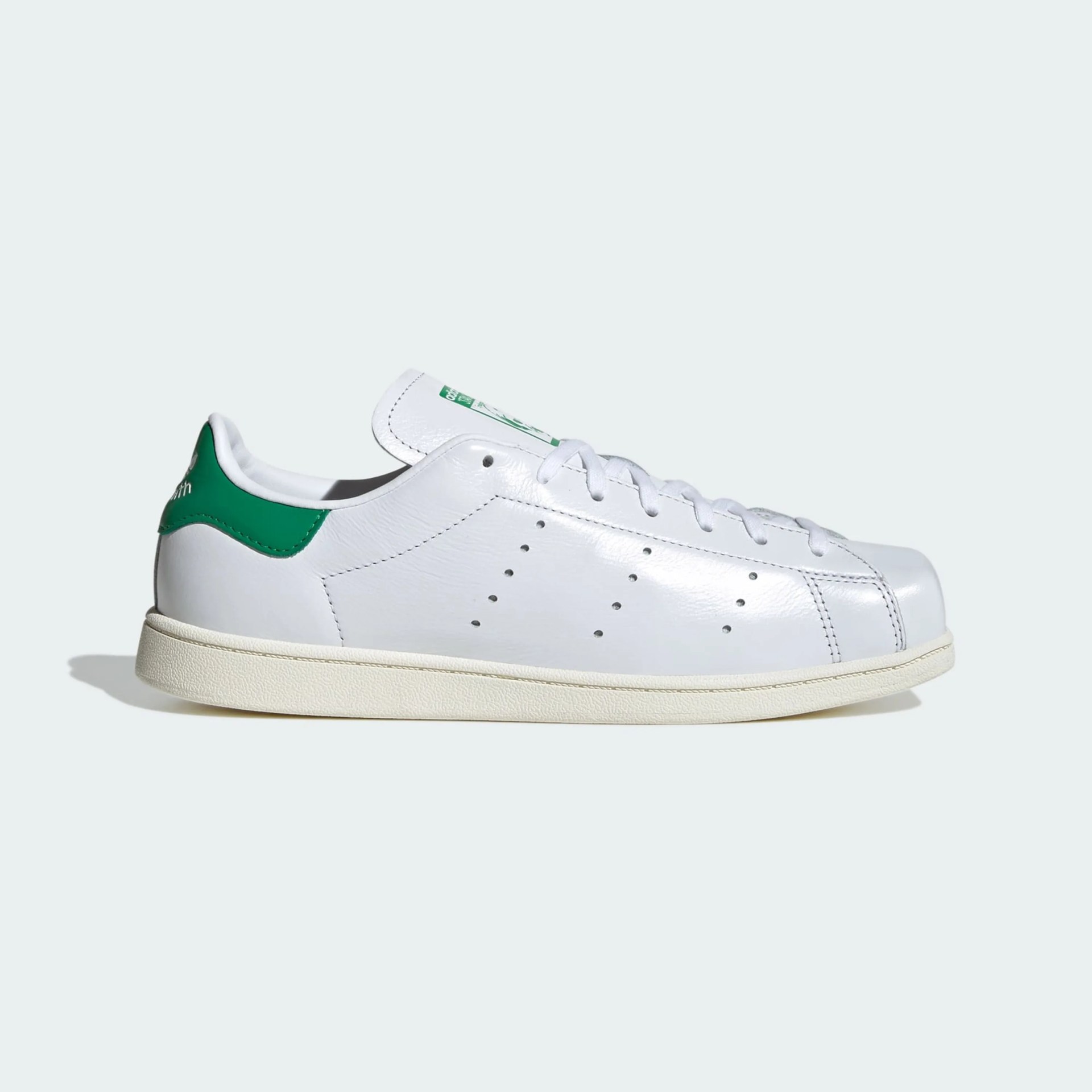 White leather sneaker with green heel tab and perforated side details on a light background.