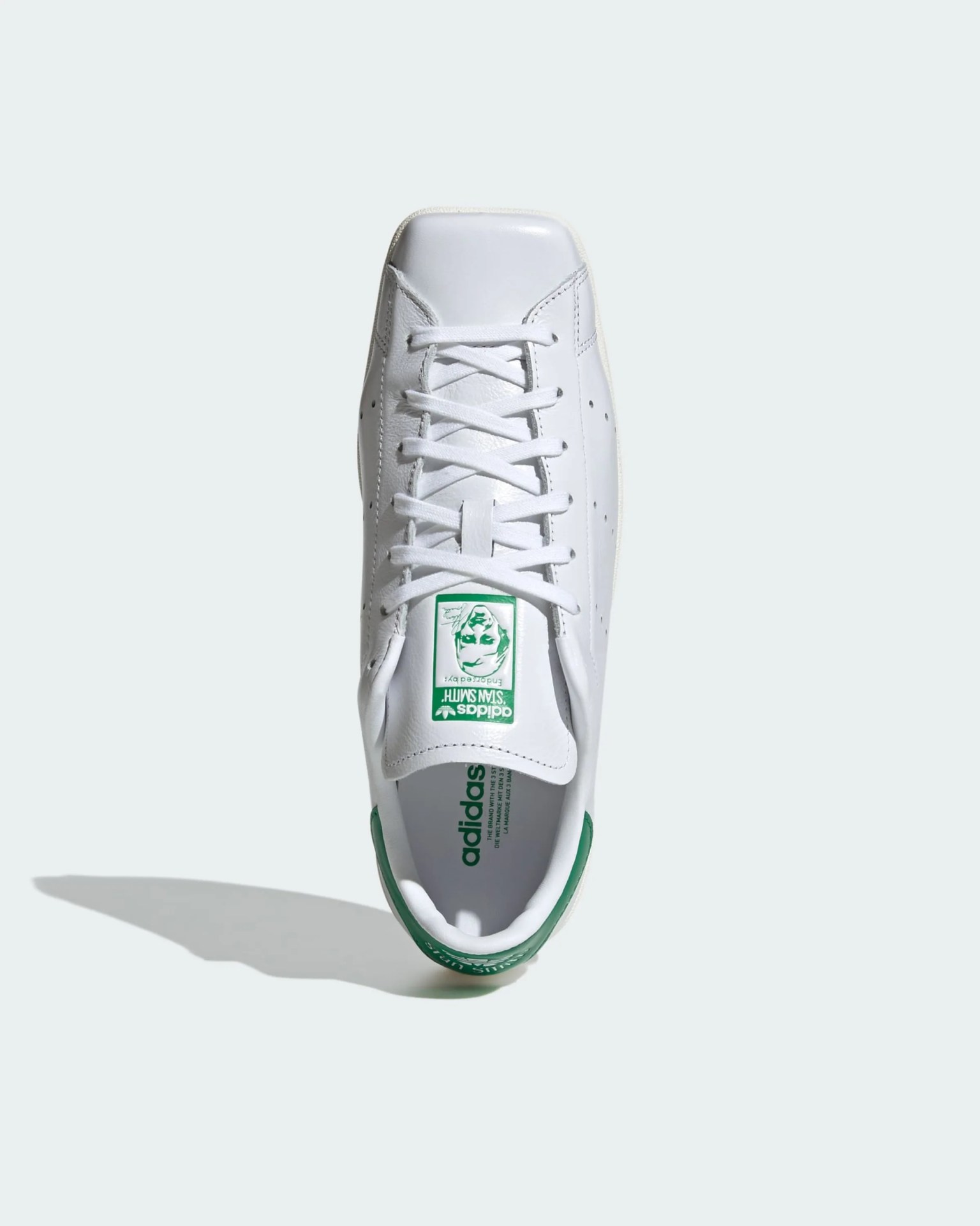 White Adidas Stan Smith sneaker with green heel tab and green logo on tongue viewed from above.