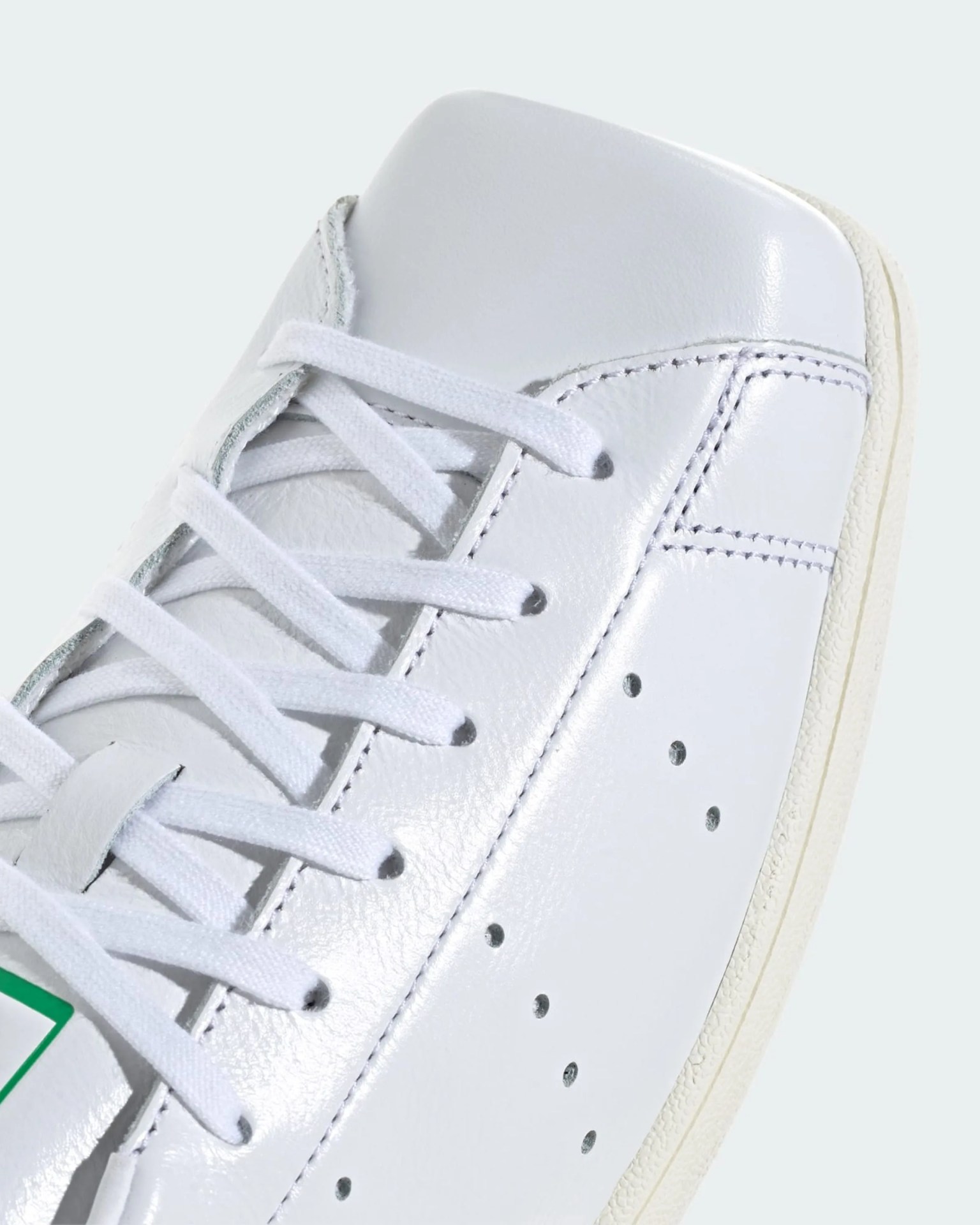 Close-up of a white leather sneaker toe with white laces and perforated side holes.