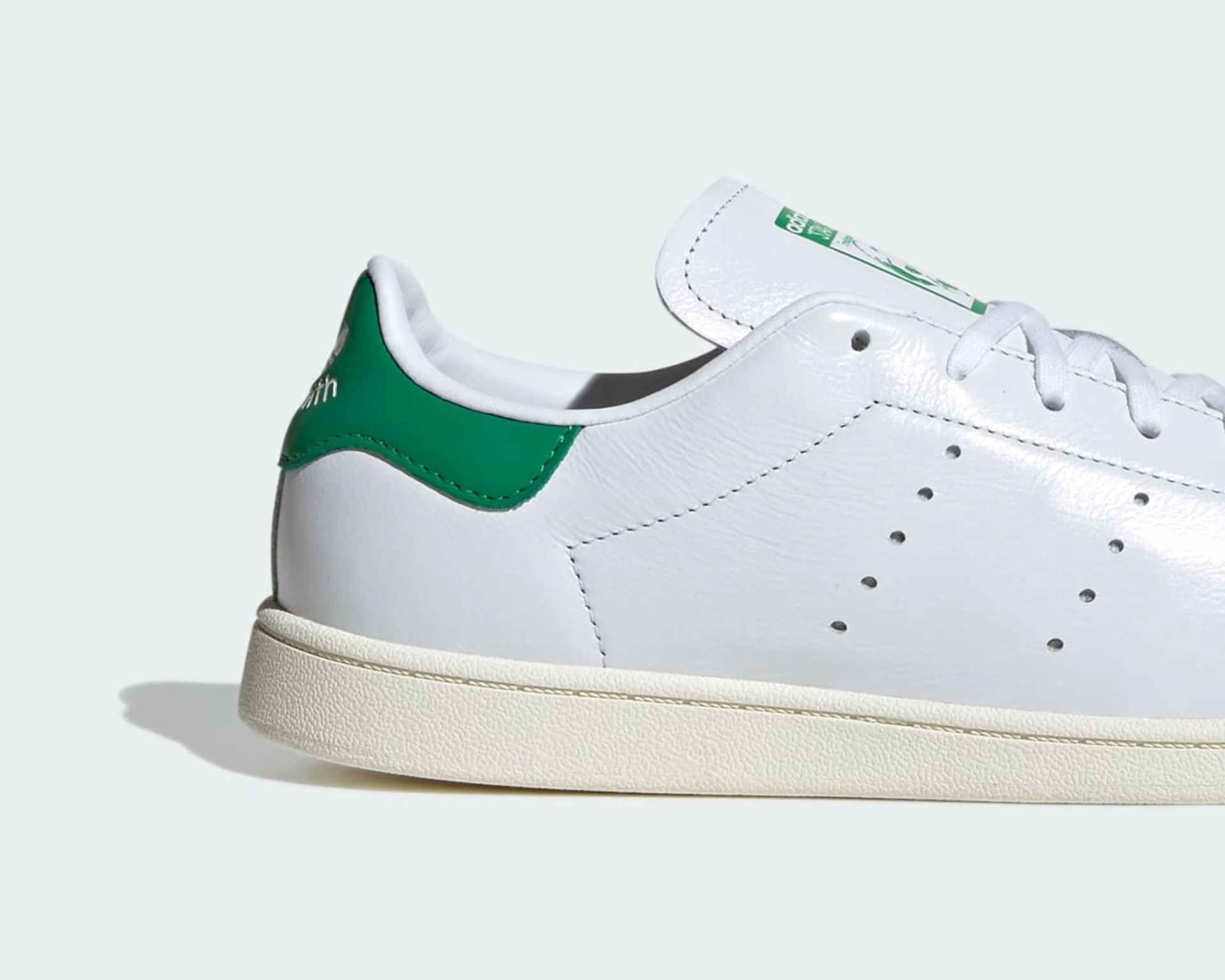 White leather sneaker with green heel tab and perforated side detail on a white background.