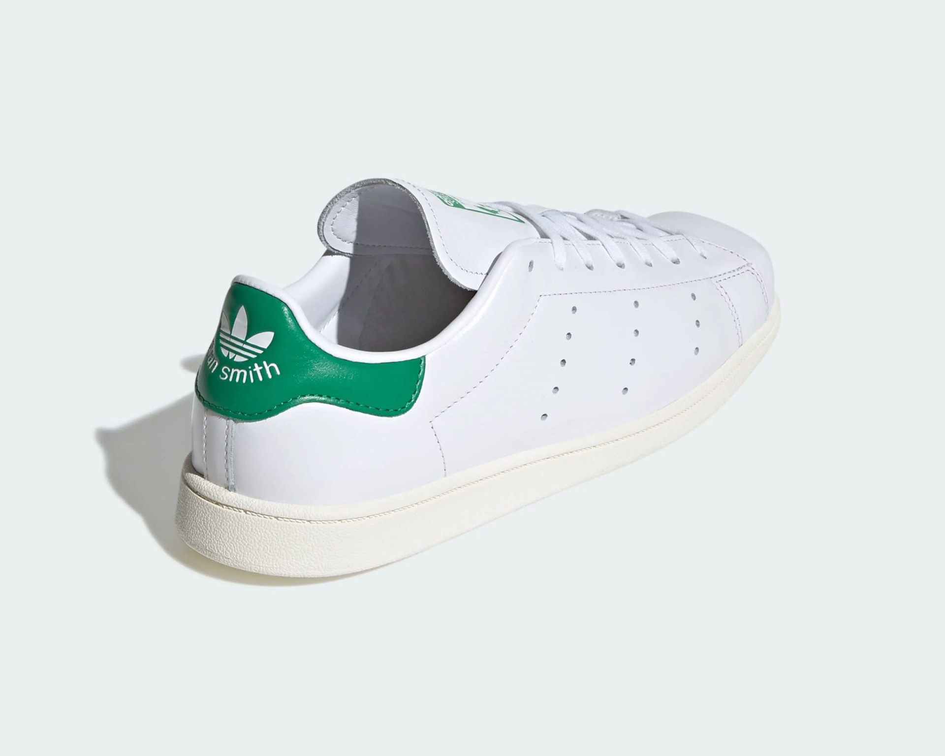 White leather Adidas Stan Smith sneaker with green heel tab and white sole on a light background.