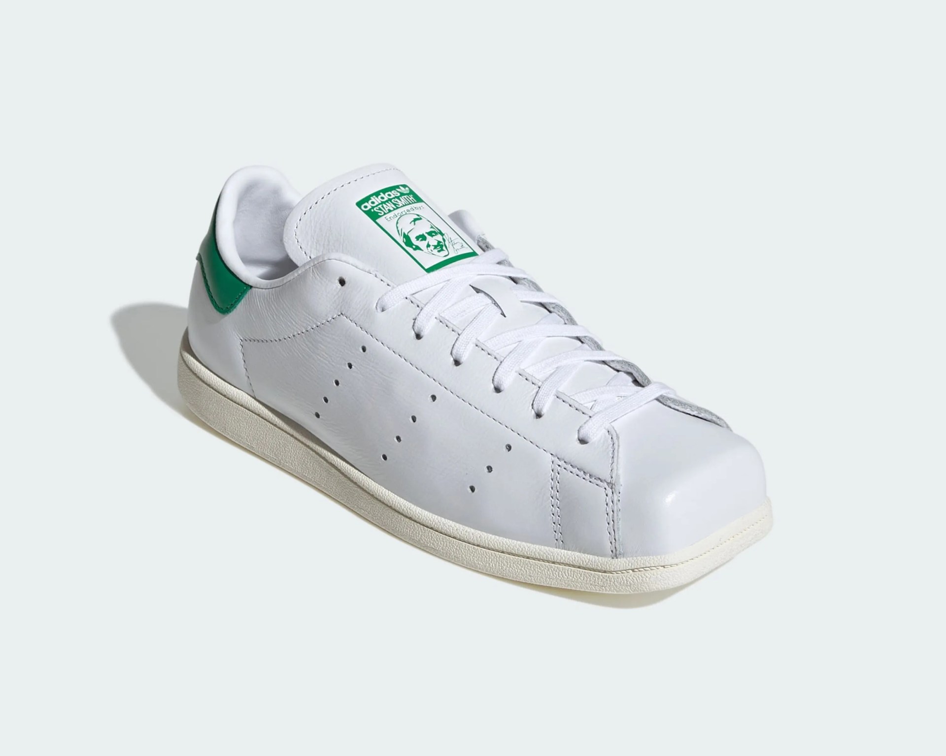 White Adidas Stan Smith sneaker with green heel tab and green logo on the tongue.