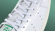 Close-up of white leather sneaker with white laces and green logo on tongue against green background.