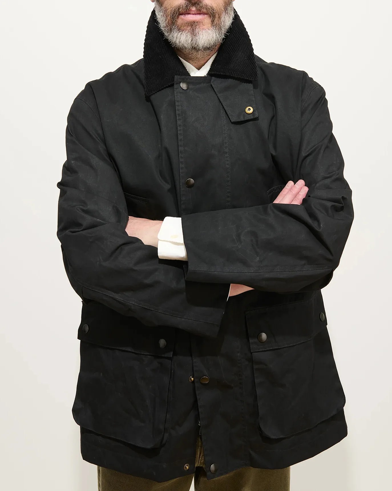 Black waxed cotton jacket with corduroy collar and snap-button flap pockets worn by a person with arms crossed.
