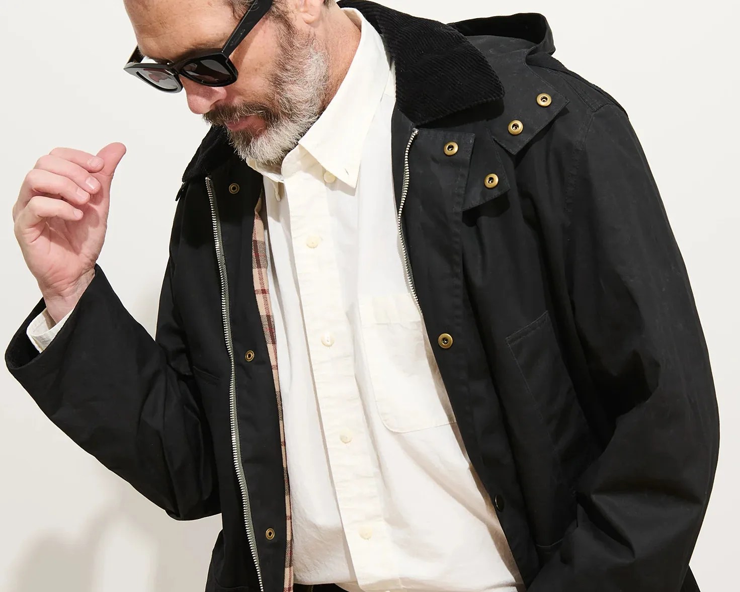 Man wearing black jacket with brass snap buttons and zipper over a white button-up shirt with a chest pocket.