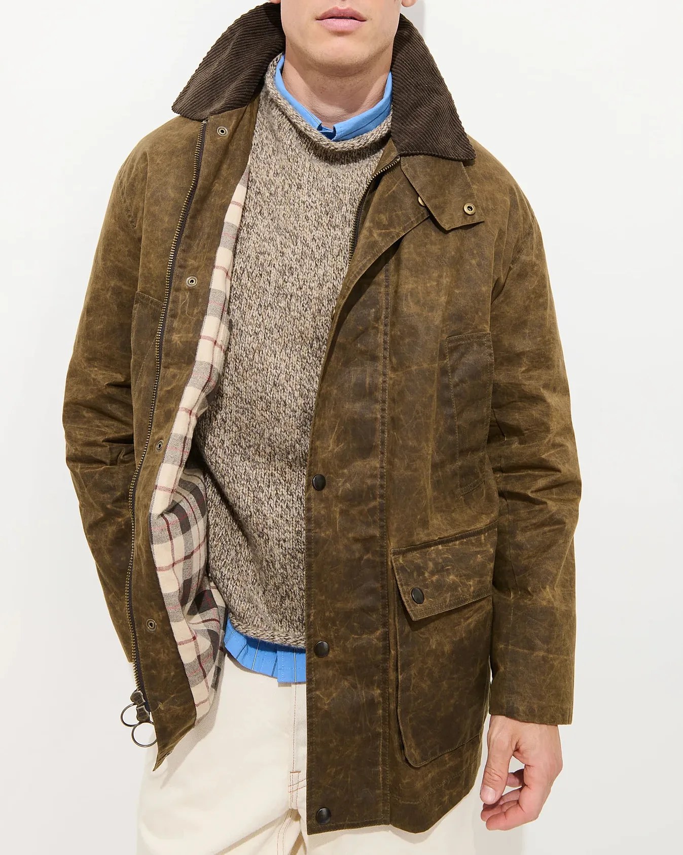 Brown waxed cotton jacket with corduroy collar and plaid lining worn over a beige knit sweater and blue shirt.