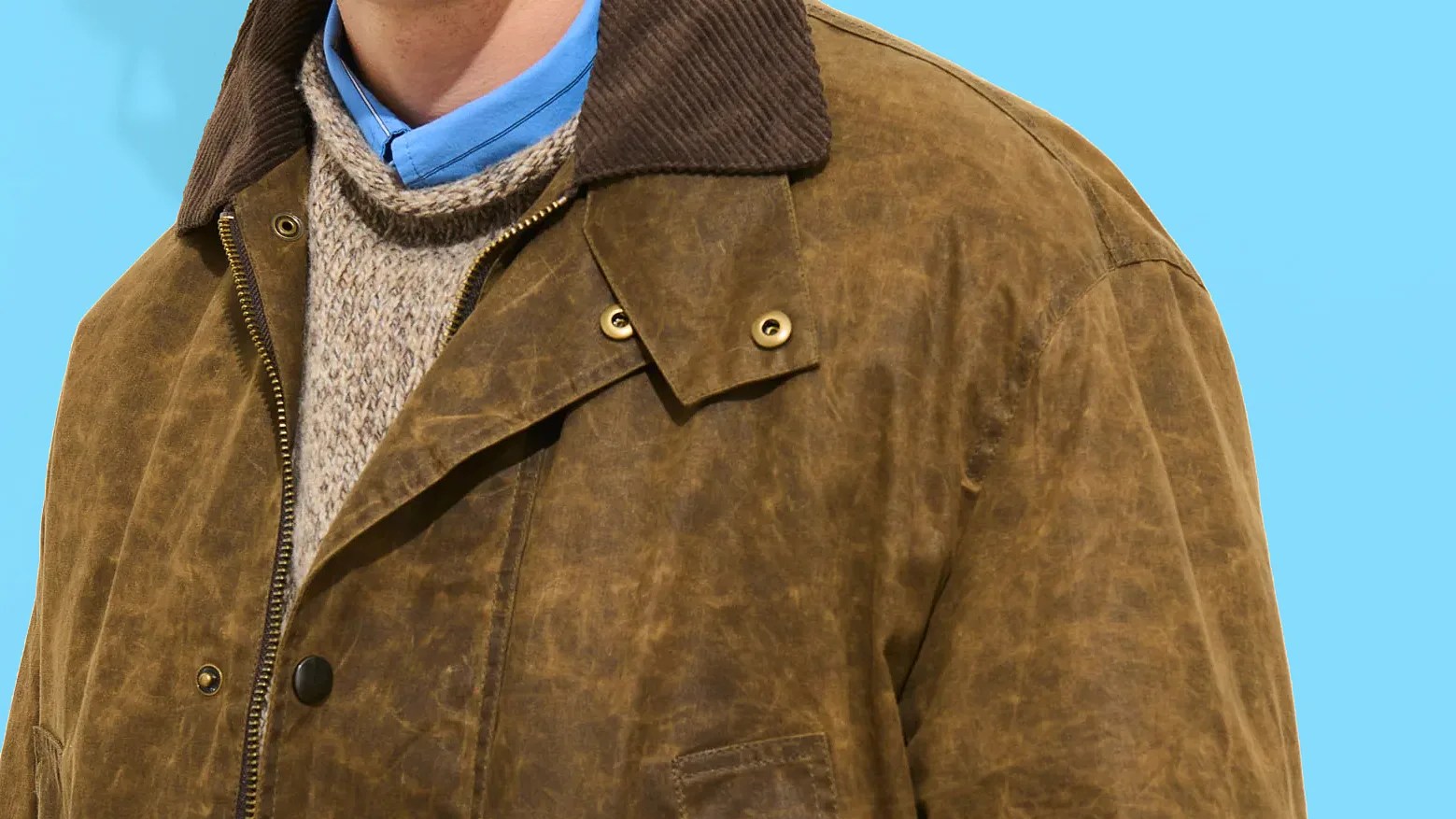 Brown waxed cotton jacket with corduroy collar worn over a beige knit sweater and blue collared shirt.